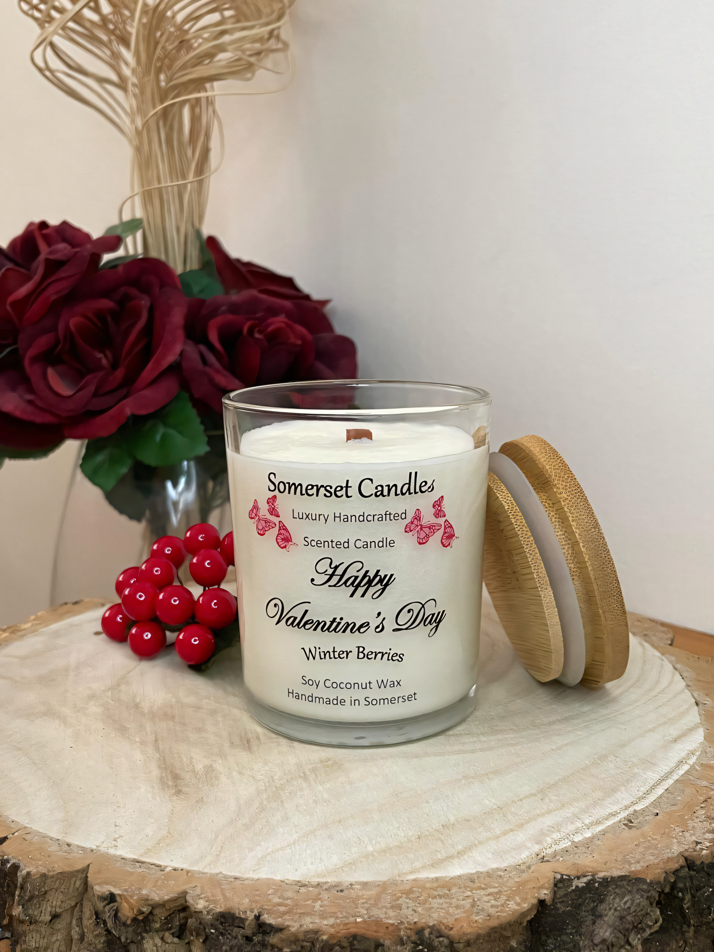 Valentines Day Candle Gift Winter Berries displayed on a wooden board with berries and roses. The candle is white in colour with bright red butterflies fluttering above the scent name. A bamboo lid is lent against the right side of the candle.