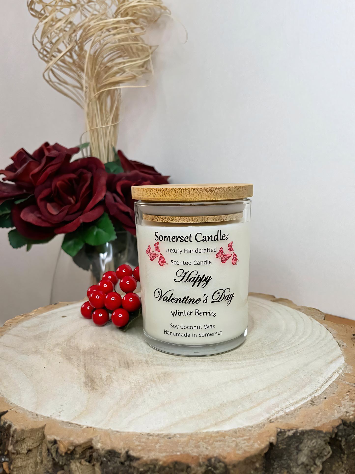 Valentines Day Candle Gift Winter Berries displayed on a wooden board with berries and roses. The candle is white in colour with bright red butterflies fluttering above the scent name. A bamboo lid is fitted to the candle.