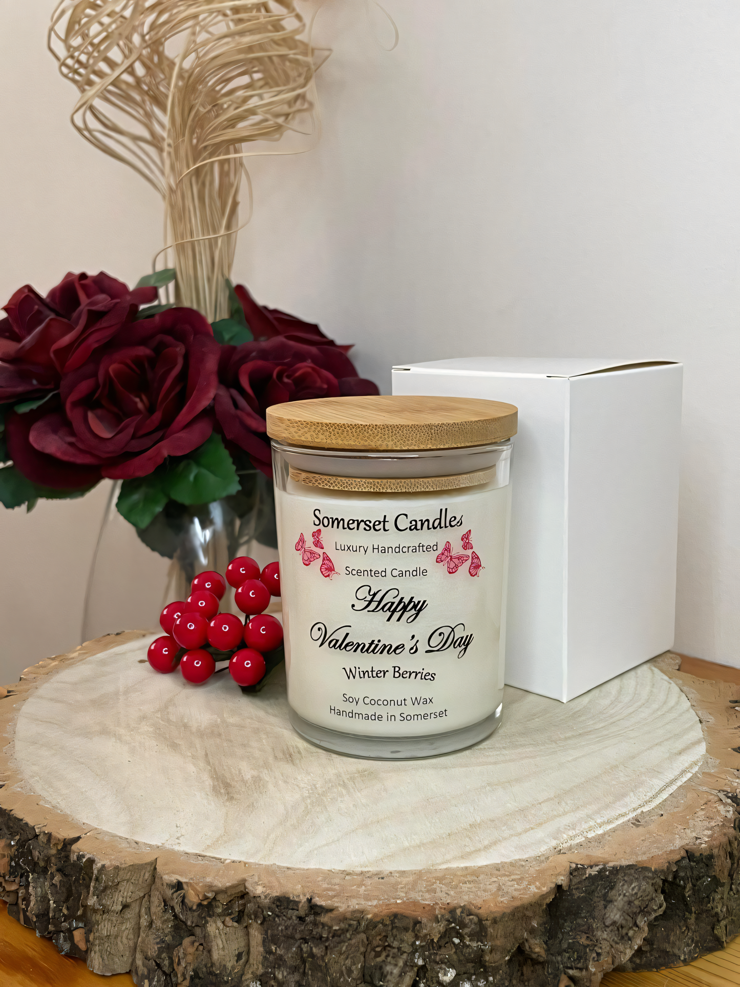 Valentines Day Candle Gift Winter Berries displayed on a wooden board with berries and roses. The candle is white in colour with bright red butterflies fluttering above the scent name. A bamboo lid is fitted to the candle and gift boxed.