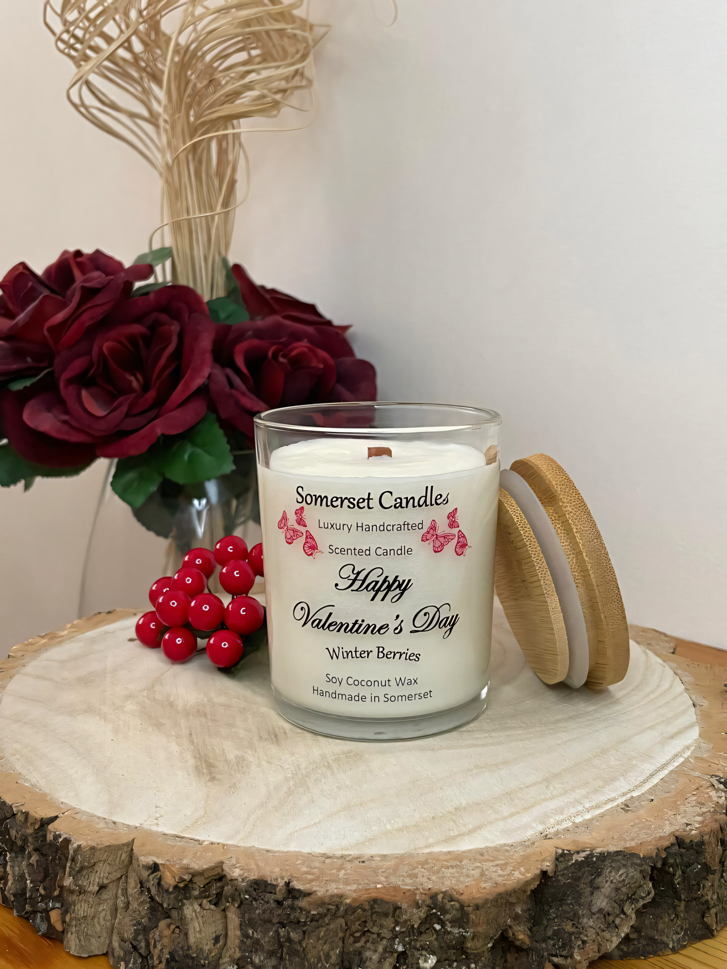 Valentines Day Candle Gift Winter Berries displayed on a wooden board with berries and roses. The candle is white in colour with bright red butterflies fluttering above the scent name and a bamboo lid.
