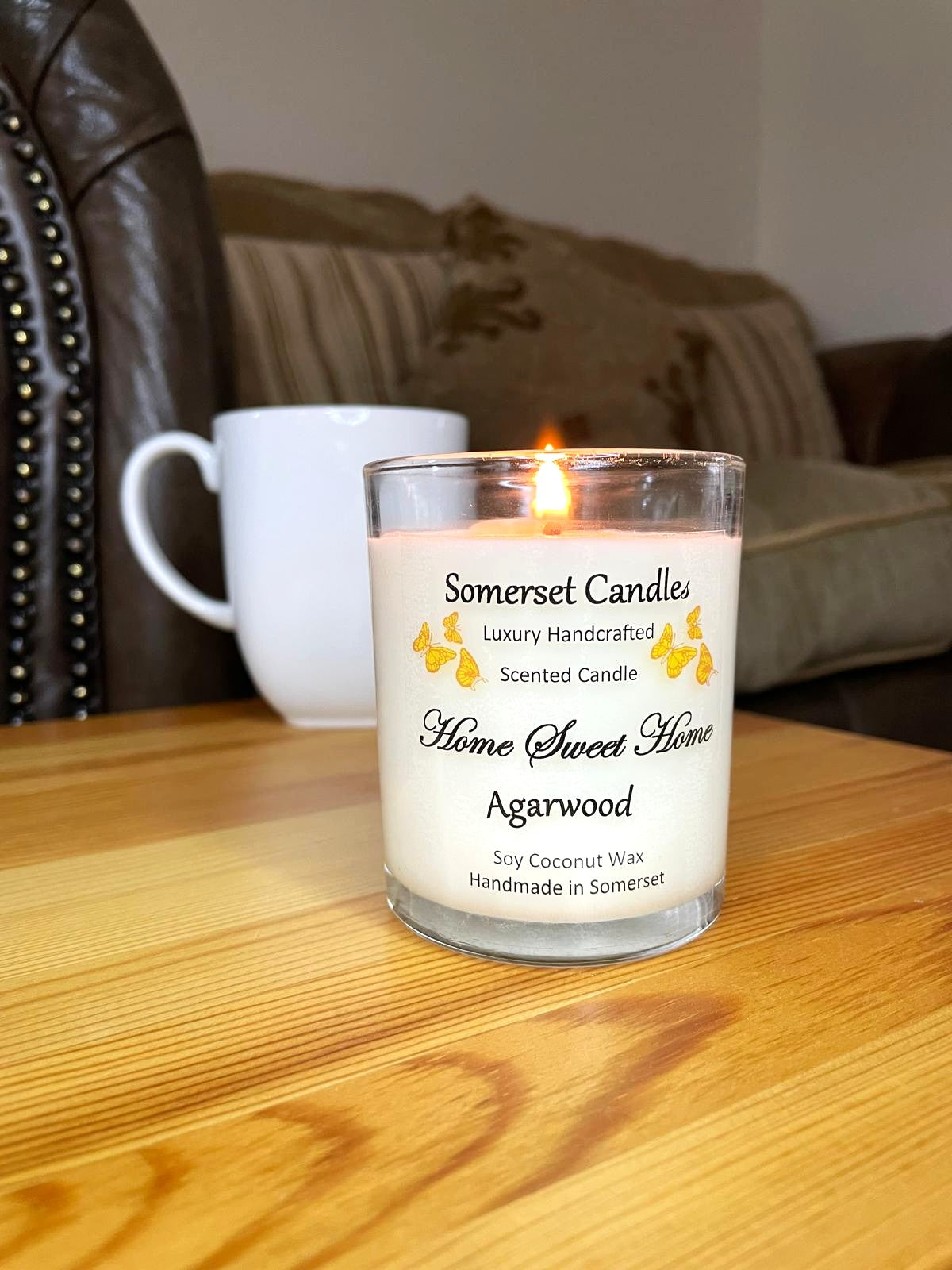 White soy candle in a 7oz clear glass jar with a natural wooden lid. The candle is made from a soy-coconut blend and scented with agarwod. Above the scent name on the label, several Orange butterflies are displayed, adding a romantic touch. Clean, minimalist design ideal for gifts, home decor or self-care.
