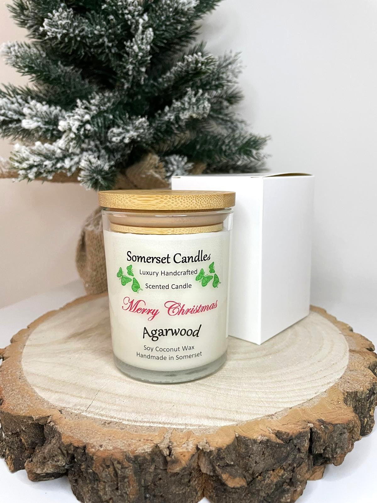 White soy candle in a 7oz clear glass jar with a natural wooden lid. The candle is made from a soy-coconut blend and scented with woodsie scent of agarwood. Above the scent name on the label, several orange butterflies are displayed, adding a romantic touch. Clean, minimalist design ideal for gifts, home decor or self-care.