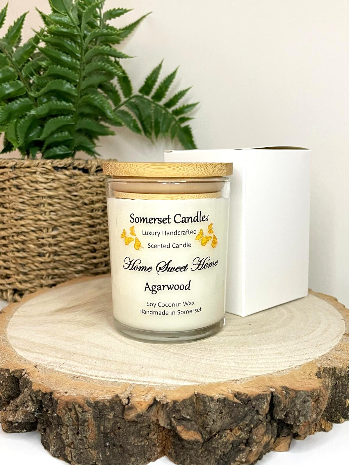 White soy candle in a 7oz clear glass jar with a natural wooden lid. The candle is made from a soy-coconut blend and scented with agarwod. Above the scent name on the label, several Orange butterflies are displayed, adding a romantic touch. Clean, minimalist design ideal for gifts, home decor or self-care.