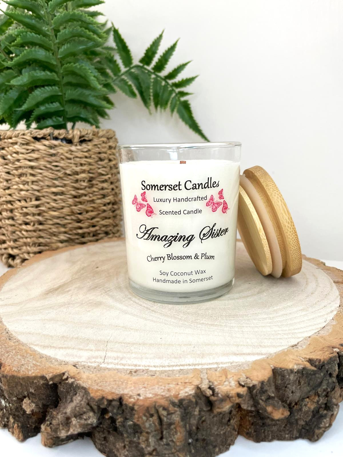 White soy candle in a 7oz clear glass jar with a natural wooden lid. The candle is made from a soy-coconut blend and scented with a delicate mix of cherry blossom and plum. Above the scent name on the label, several red butterflies are displayed, adding a romantic touch. Clean, minimalist design ideal for gifts, home decor or self-care.
