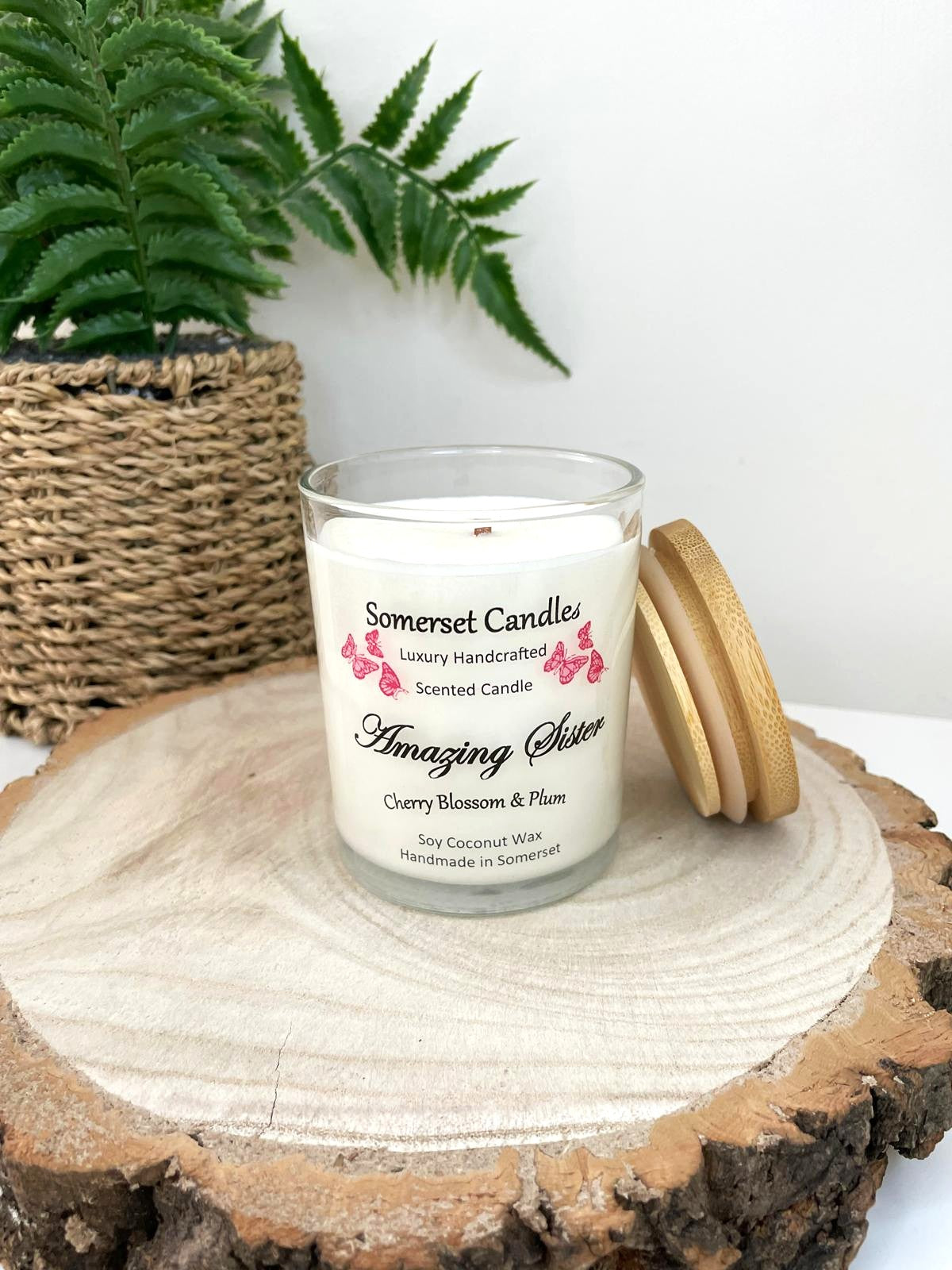 White soy candle in a 7oz clear glass jar with a natural wooden lid. The candle is made from a soy-coconut blend and scented with a delicate mix of cherry blossom and plum. Above the scent name on the label, several red butterflies are displayed, adding a romantic touch. Clean, minimalist design ideal for gifts, home decor or self-care.