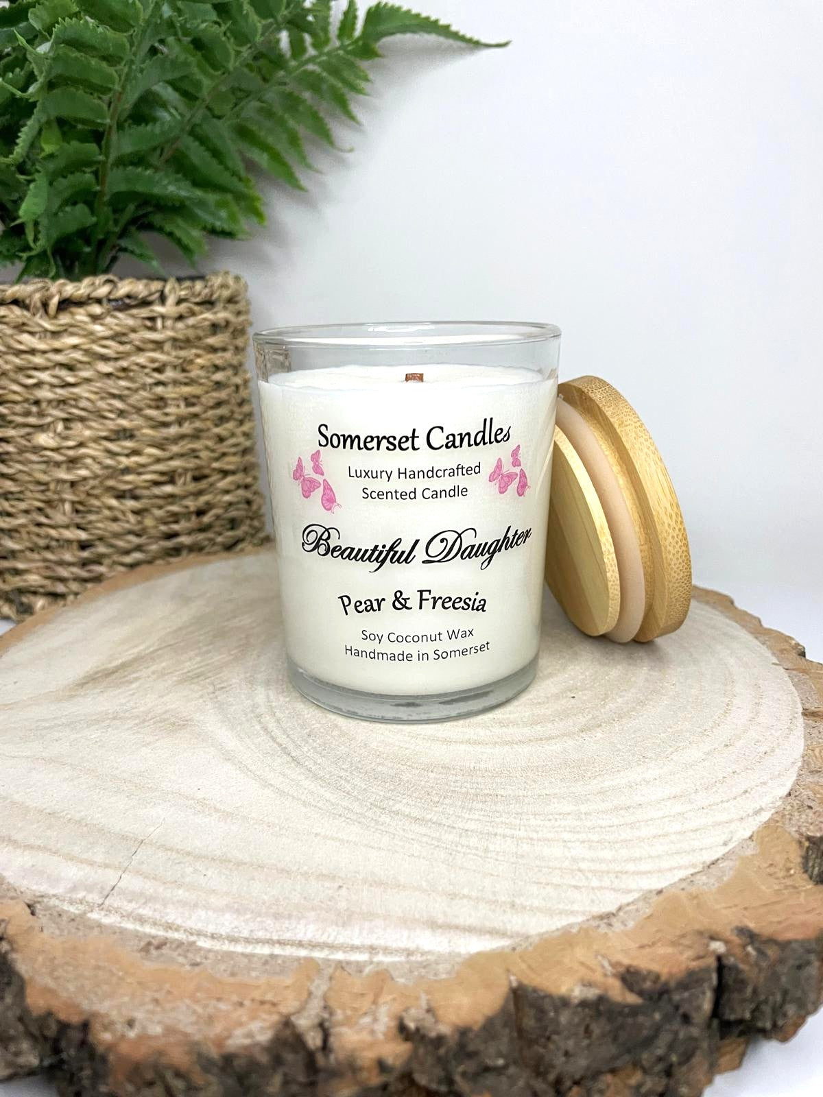 White soy candle in a 7oz clear glass jar with a natural wooden lid. The candle is made from a soy-coconut blend and scented with a delicate mix of pear and freesia. Above the scent name on the label, several pink butterflies are displayed, adding a romantic touch. Clean, minimalist design ideal for gifts, home decor or self-care.