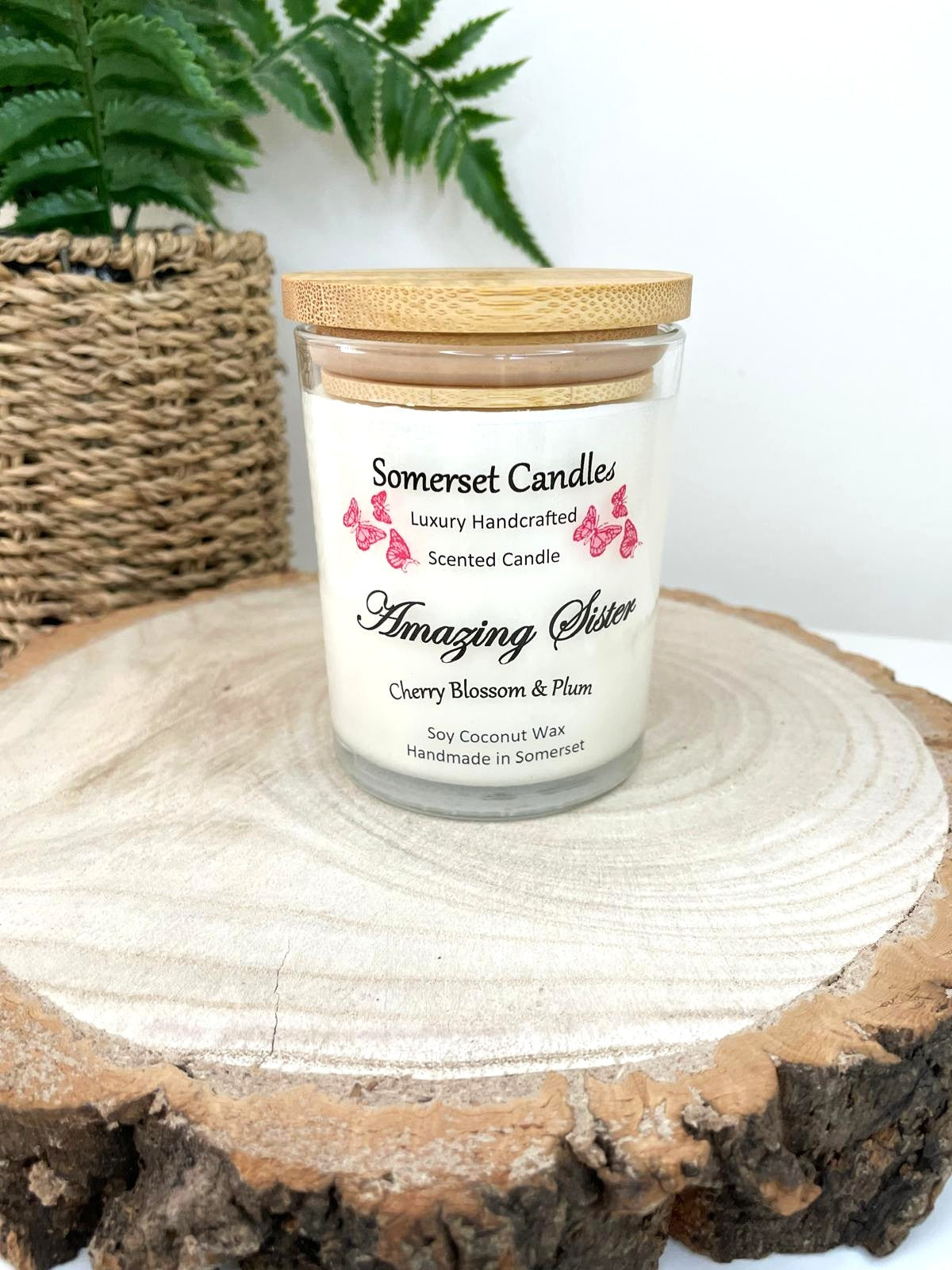 White soy candle in a 7oz clear glass jar with a natural wooden lid. The candle is made from a soy-coconut blend and scented with a delicate mix of cherry blossom and plum. Above the scent name on the label, several red butterflies are displayed, adding a romantic touch. Clean, minimalist design ideal for gifts, home decor or self-care.