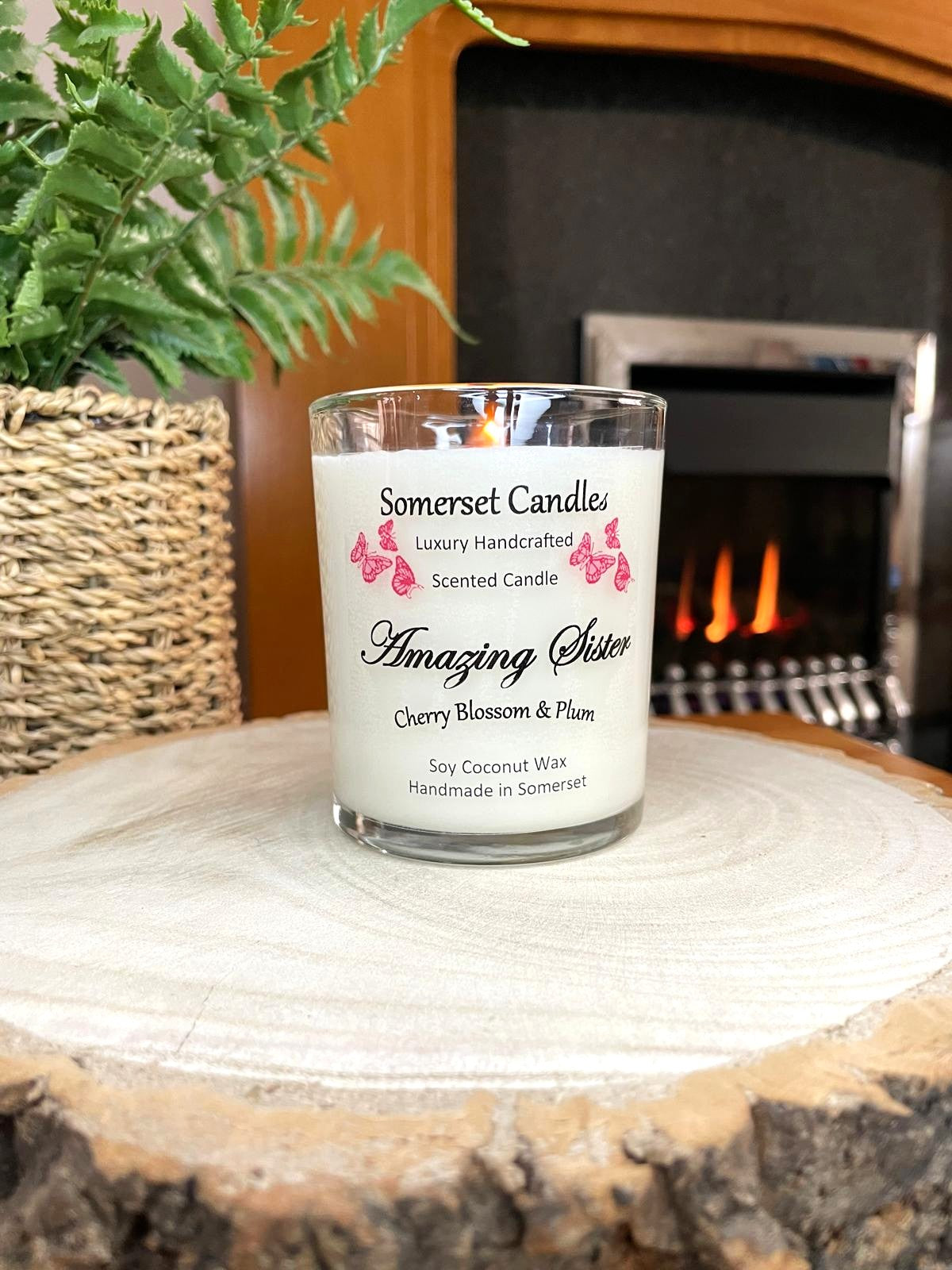 White soy candle in a 7oz clear glass jar with a natural wooden lid. The candle is made from a soy-coconut blend and scented with a delicate mix of cherry blossom and plum. Above the scent name on the label, several red butterflies are displayed, adding a romantic touch. Clean, minimalist design ideal for gifts, home decor or self-care.