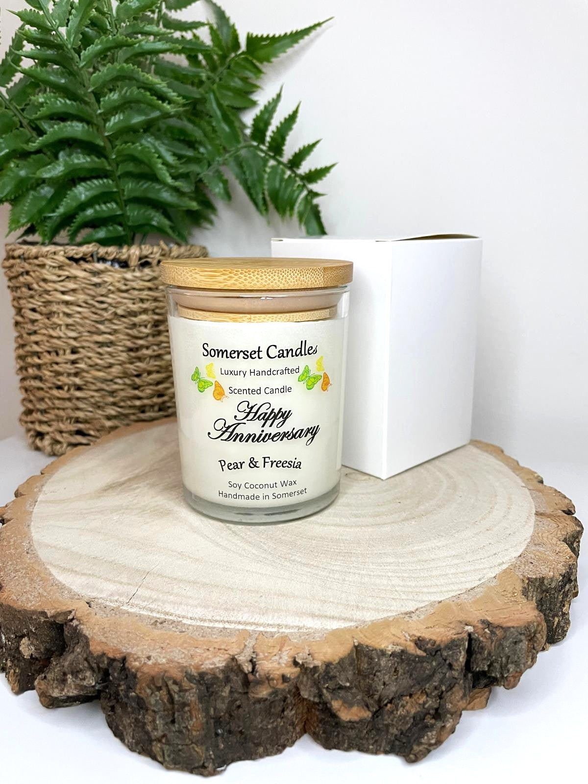 White soy candle in a 7oz clear glass jar with a natural wooden lid. The candle is made from a soy-coconut blend and scented with a delicate fruity floral scent of pear and freesia. Above the scent name on the label, several yellow, green and orange butterflies are displayed, adding a romantic touch. Clean, minimalist design ideal for gifts, home decor or self-care.