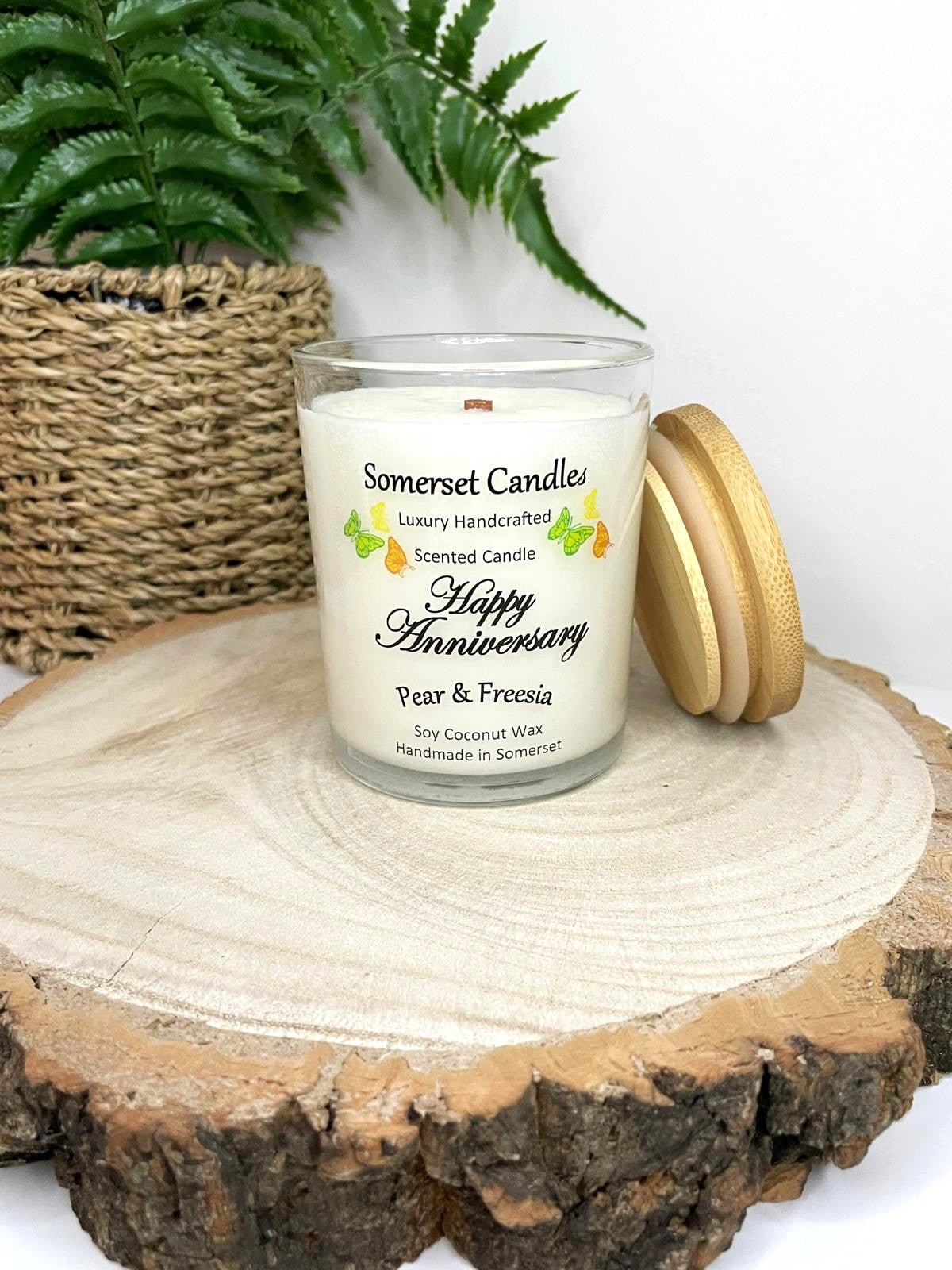 White soy candle in a 7oz clear glass jar with a natural wooden lid. The candle is made from a soy-coconut blend and scented with a delicate fruity floral scent of pear and freesia. Above the scent name on the label, several yellow, green and orange butterflies are displayed, adding a romantic touch. Clean, minimalist design ideal for gifts, home decor or self-care.