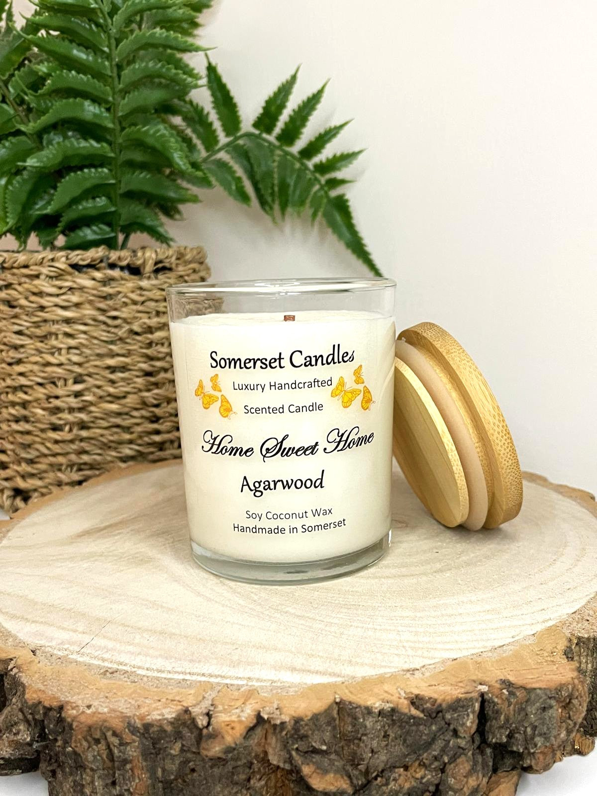 White soy candle in a 7oz clear glass jar with a natural wooden lid. The candle is made from a soy-coconut blend and scented with agarwod. Above the scent name on the label, several Orange butterflies are displayed, adding a romantic touch. Clean, minimalist design ideal for gifts, home decor or self-care.
