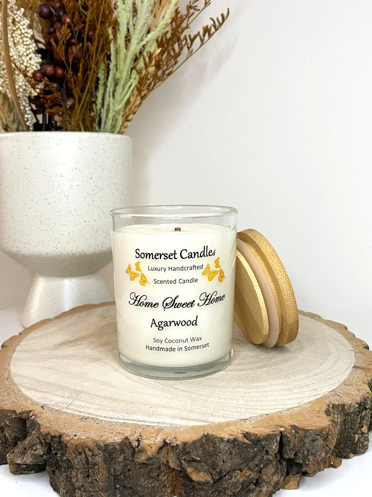 White soy candle in a 7oz clear glass jar with a natural wooden lid. The candle is made from a soy-coconut blend and scented with agarwod. Above the scent name on the label, several Orange butterflies are displayed, adding a romantic touch. Clean, minimalist design ideal for gifts, home decor or self-care.