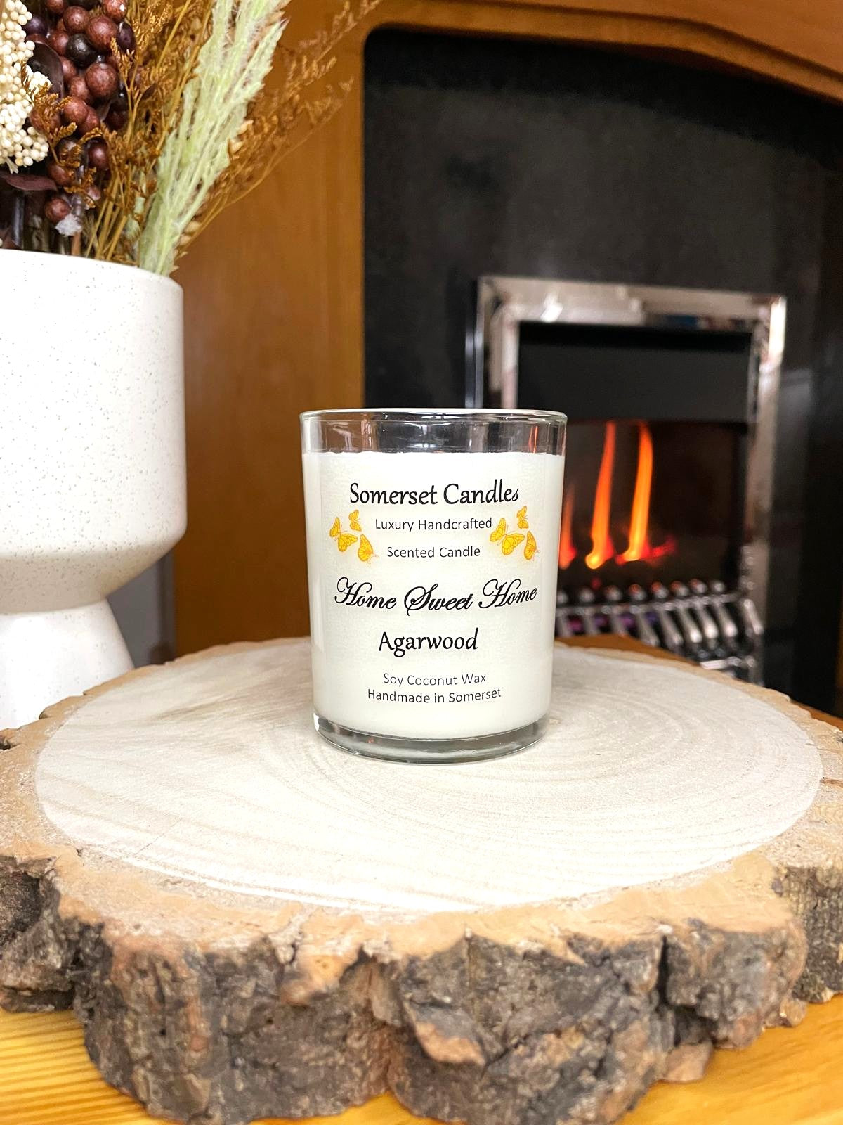 White soy candle in a 7oz clear glass jar with a natural wooden lid. The candle is made from a soy-coconut blend and scented with agarwod. Above the scent name on the label, several Orange butterflies are displayed, adding a romantic touch. Clean, minimalist design ideal for gifts, home decor or self-care.
