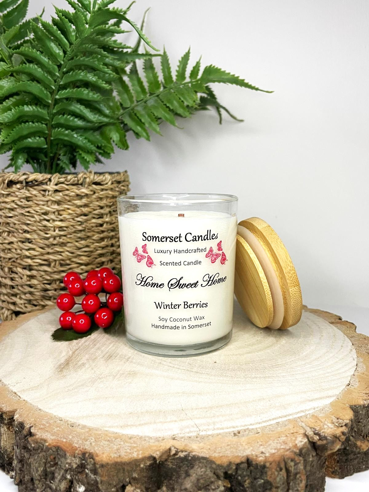 White soy candle in a 7oz clear glass jar with a natural wooden lid. The candle is made from a soy-coconut blend and scented with fruity winter berries. Above the scent name on the label, several red butterflies are displayed, adding a romantic touch. Clean, minimalist design ideal for gifts, home decor or self-care.