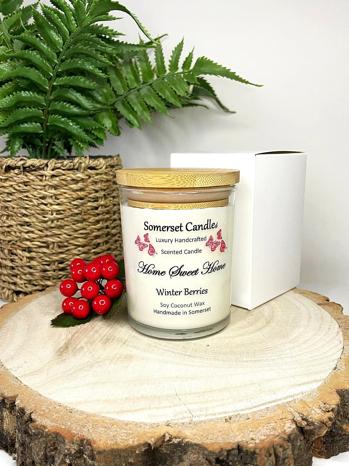 White soy candle in a 7oz clear glass jar with a natural wooden lid. The candle is made from a soy-coconut blend and scented with fruity winter berries. Above the scent name on the label, several red butterflies are displayed, adding a romantic touch. Clean, minimalist design ideal for gifts, home decor or self-care.