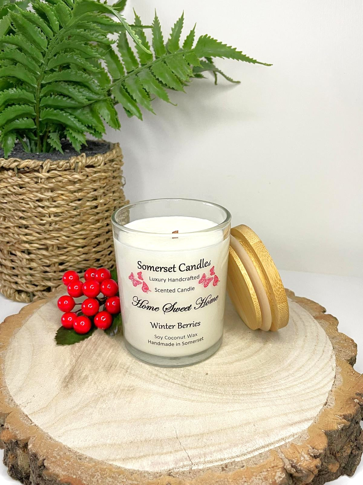 White soy candle in a 7oz clear glass jar with a natural wooden lid. The candle is made from a soy-coconut blend and scented with fruity winter berries. Above the scent name on the label, several red butterflies are displayed, adding a romantic touch. Clean, minimalist design ideal for gifts, home decor or self-care.