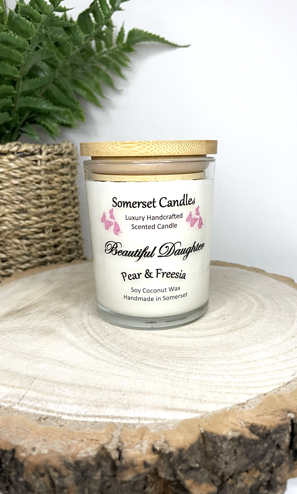White soy candle in a 7oz clear glass jar with a natural wooden lid. The candle is made from a soy-coconut blend and scented with a delicate mix of pear and freesia. Above the scent name on the label, several pink butterflies are displayed, adding a romantic touch. Clean, minimalist design ideal for gifts, home decor or self-care.