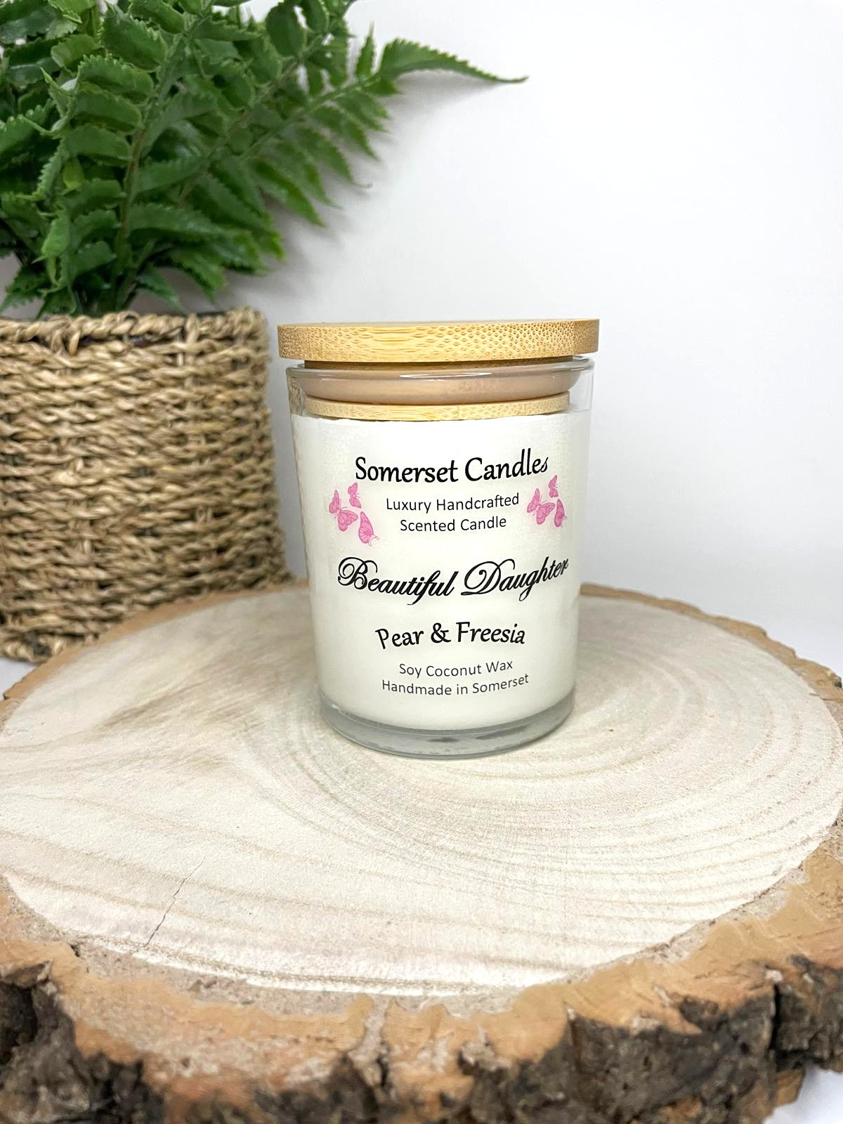 White soy candle in a 7oz clear glass jar with a natural wooden lid. The candle is made from a soy-coconut blend and scented with a delicate mix of pear and freesia. Above the scent name on the label, several pink butterflies are displayed, adding a romantic touch. Clean, minimalist design ideal for gifts, home decor or self-care.
