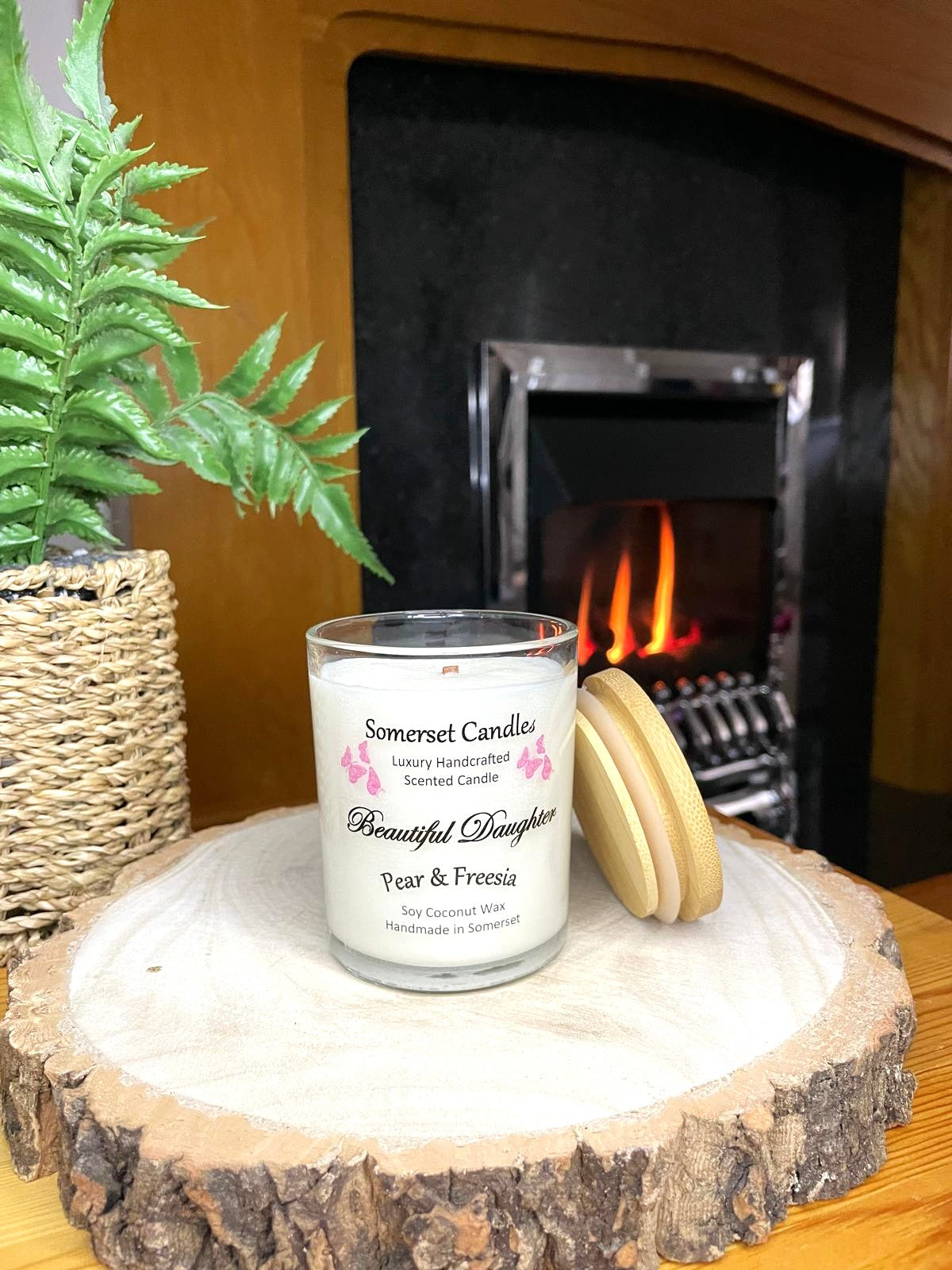 White soy candle in a 7oz clear glass jar with a natural wooden lid. The candle is made from a soy-coconut blend and scented with a delicate mix of pear and freesia. Above the scent name on the label, several pink butterflies are displayed, adding a romantic touch. Clean, minimalist design ideal for gifts, home decor or self-care.
