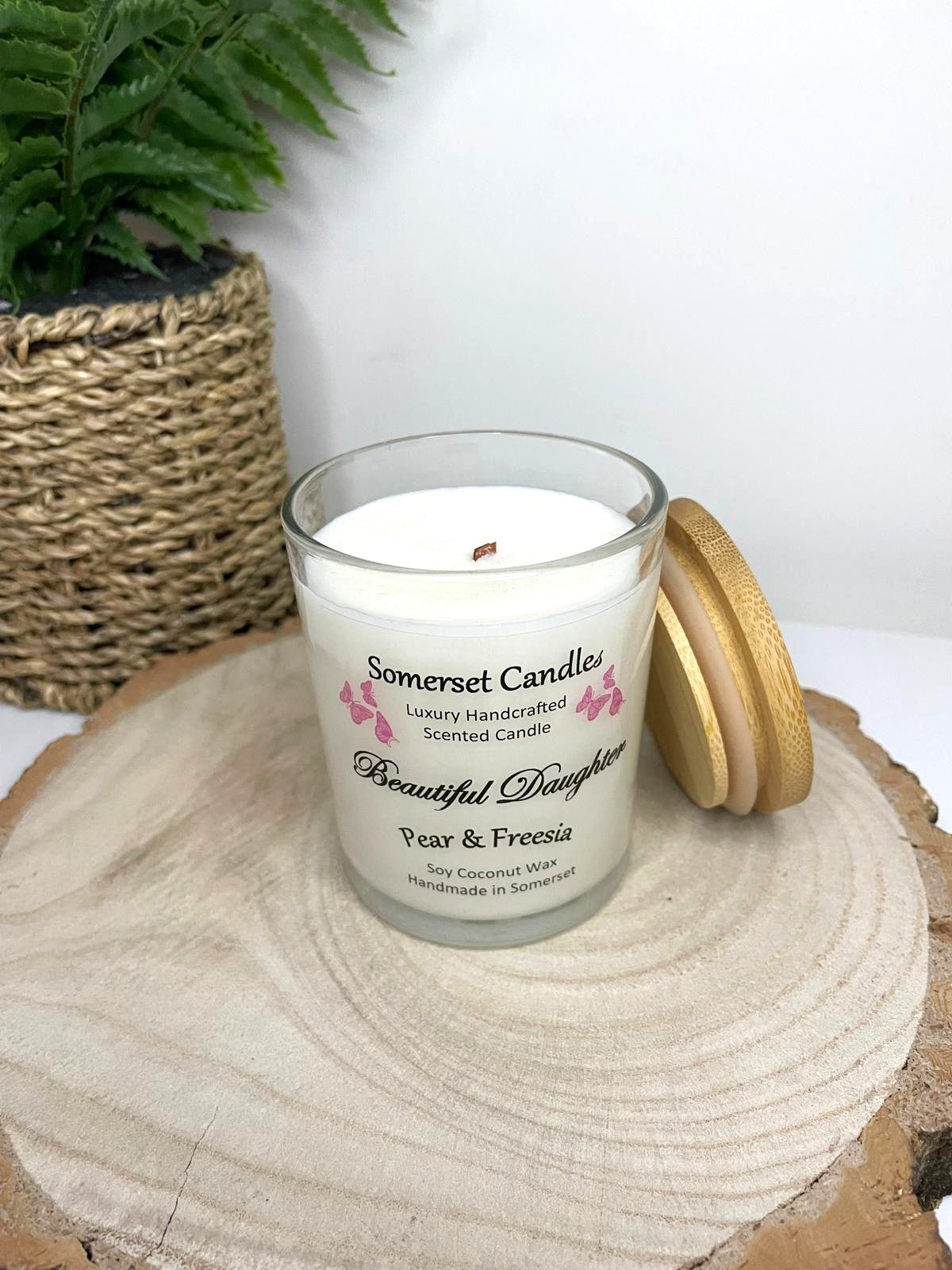 White soy candle in a 7oz clear glass jar with a natural wooden lid. The candle is made from a soy-coconut blend and scented with a delicate mix of pear and freesia. Above the scent name on the label, several pink butterflies are displayed, adding a romantic touch. Clean, minimalist design ideal for gifts, home decor or self-care.