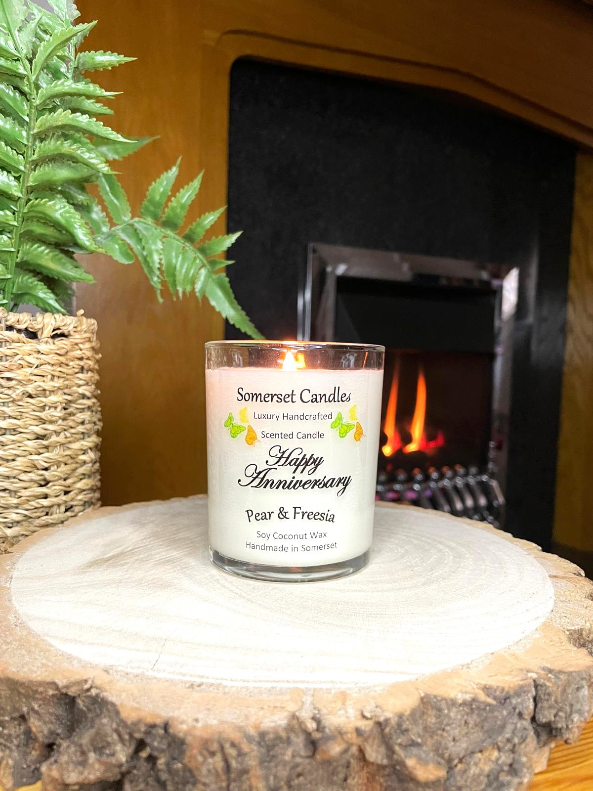 White soy candle in a 7oz clear glass jar with a natural wooden lid. The candle is made from a soy-coconut blend and scented with a delicate fruity floral scent of pear and freesia. Above the scent name on the label, several yellow, green and orange butterflies are displayed, adding a romantic touch. Clean, minimalist design ideal for gifts, home decor or self-care.