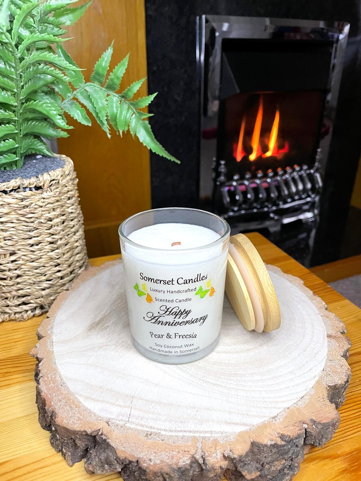 White soy candle in a 7oz clear glass jar with a natural wooden lid. The candle is made from a soy-coconut blend and scented with a delicate fruity floral scent of pear and freesia. Above the scent name on the label, several yellow, green and orange butterflies are displayed, adding a romantic touch. Clean, minimalist design ideal for gifts, home decor or self-care.