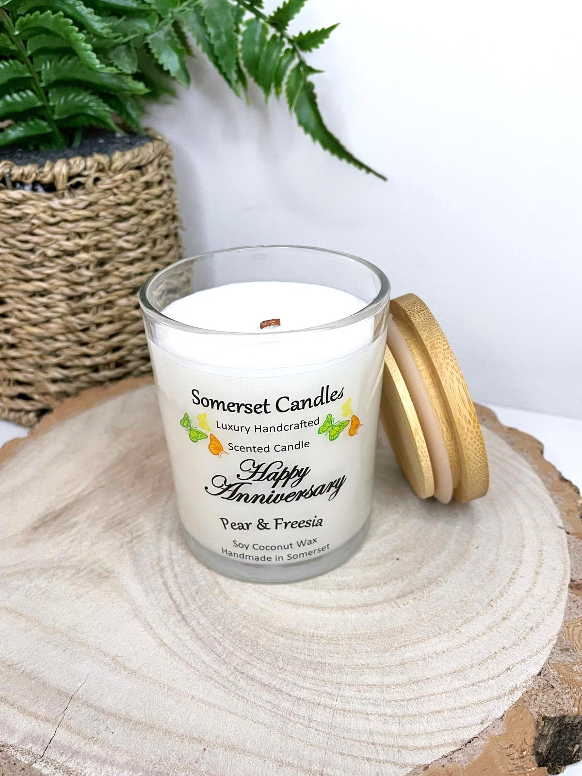 White soy candle in a 7oz clear glass jar with a natural wooden lid. The candle is made from a soy-coconut blend and scented with a delicate fruity floral scent of pear and freesia. Above the scent name on the label, several yellow, green and orange butterflies are displayed, adding a romantic touch. Clean, minimalist design ideal for gifts, home decor or self-care.