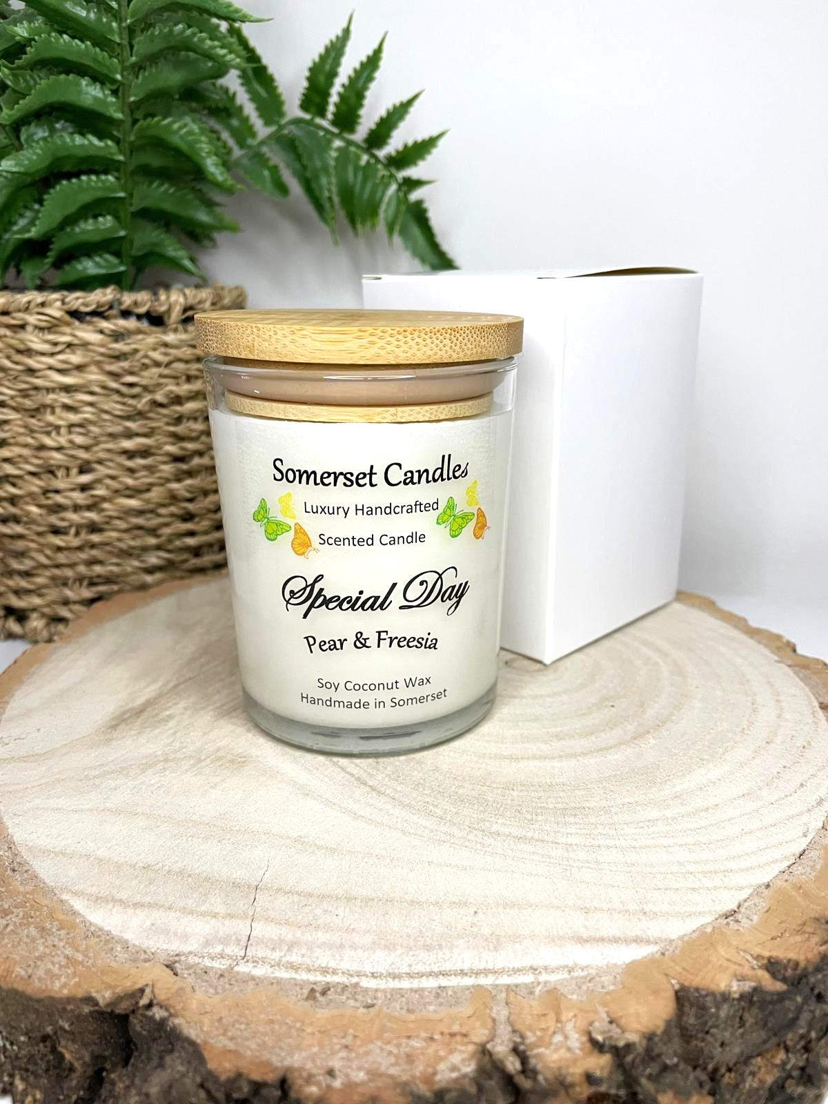 White soy candle in a 7oz clear glass jar with a natural wooden lid. The candle is made from a soy-coconut blend and scented with a delicate fruity floral scent of pear and freesia. Above the scent name on the label, several yellow, green and orange butterflies are displayed, adding a romantic touch. Clean, minimalist design ideal for gifts, home decor or self-care.