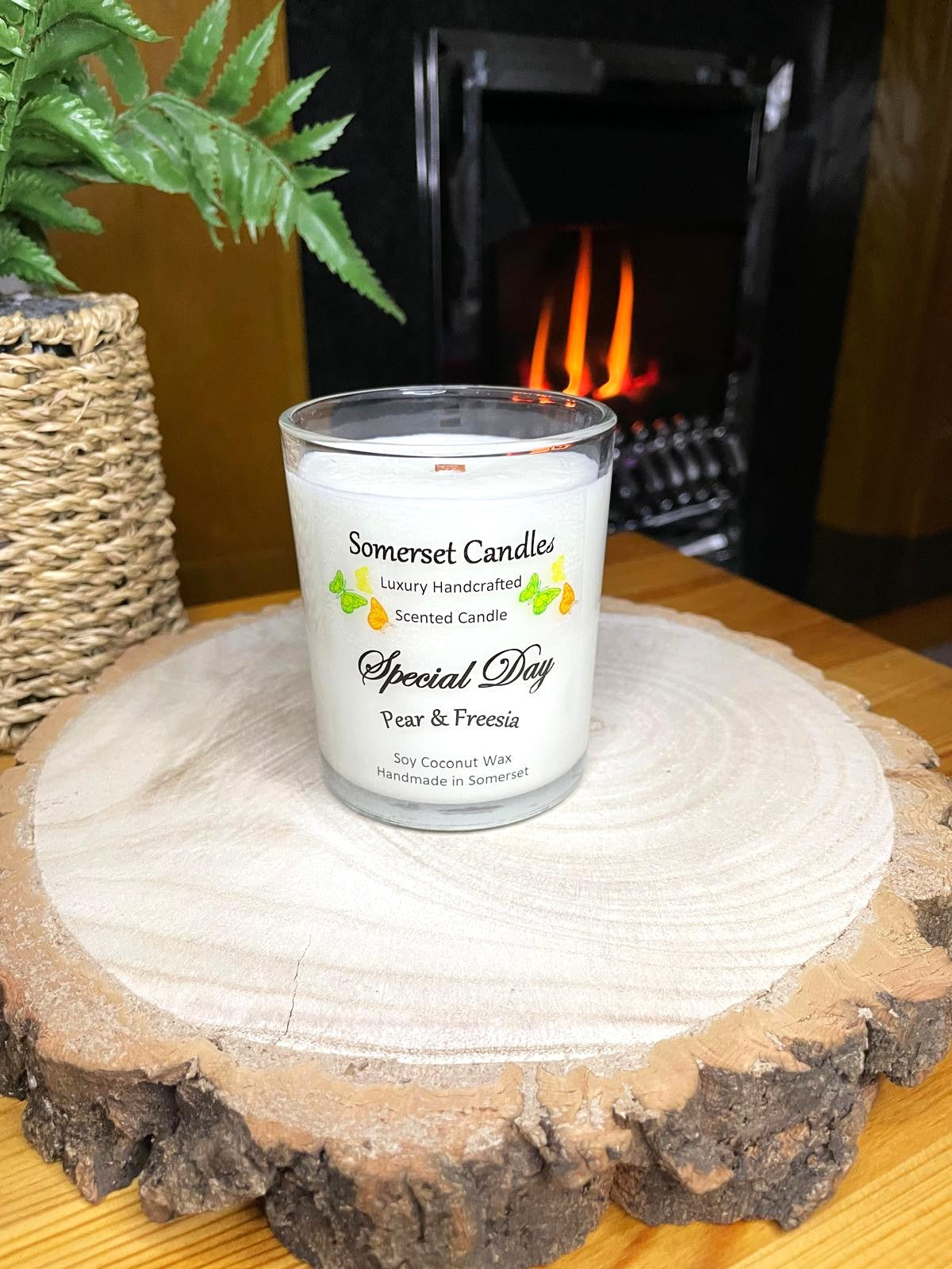 White soy candle in a 7oz clear glass jar with a natural wooden lid. The candle is made from a soy-coconut blend and scented with a delicate fruity floral scent of pear and freesia. Above the scent name on the label, several yellow, green and orange butterflies are displayed, adding a romantic touch. Clean, minimalist design ideal for gifts, home decor or self-care.