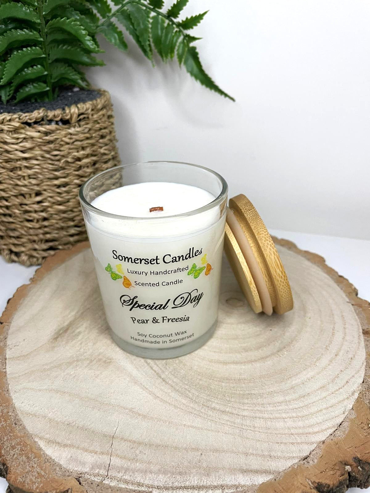 White soy candle in a 7oz clear glass jar with a natural wooden lid. The candle is made from a soy-coconut blend and scented with a delicate fruity floral scent of pear and freesia. Above the scent name on the label, several yellow, green and orange butterflies are displayed, adding a romantic touch. Clean, minimalist design ideal for gifts, home decor or self-care.