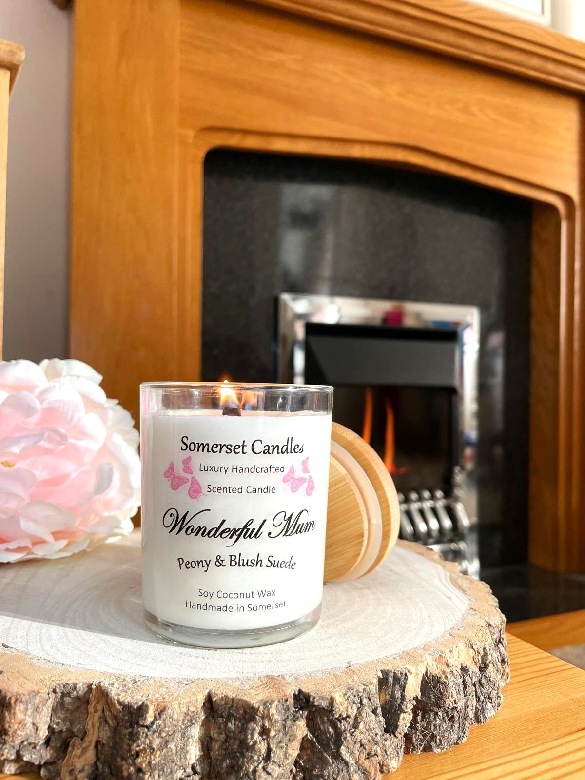 White soy candle in a 7oz clear glass jar with a natural wooden lid. The candle is made from a soy-coconut blend and scented with a delicate mix of peony and blush suede. Above the scent name on the label, several pink butterflies are displayed, adding a romantic touch. Clean, minimalist design ideal for gifts, home decor or self-care.