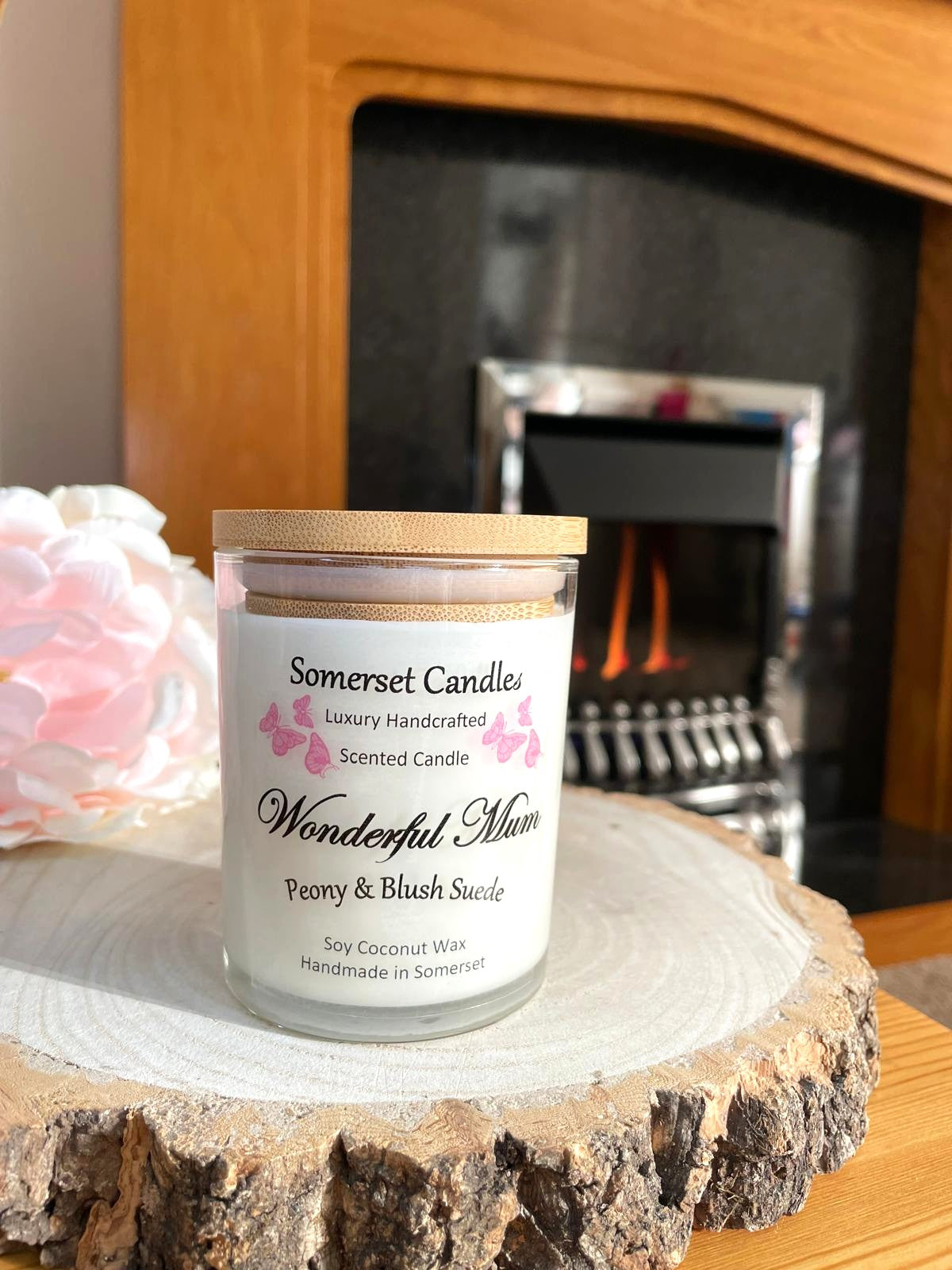 White soy candle in a 7oz clear glass jar with a natural wooden lid. The candle is made from a soy-coconut blend and scented with a delicate mix of peony and blush suede. Above the scent name on the label, several pink butterflies are displayed, adding a romantic touch. Clean, minimalist design ideal for gifts, home decor or self-care.