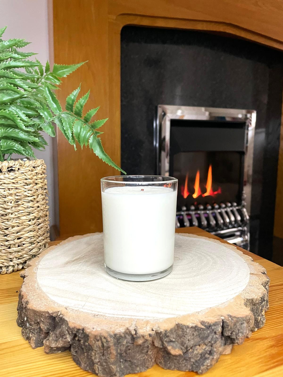 White soy candle in a 7oz clear glass jar with a natural wooden lid. The candle is made from a soy-coconut blend and a variety of fresh fragrances. The candle has no label. The candle is in front of a lit fire. Clean, minimalist design ideal for gifts, home decor or self-care.