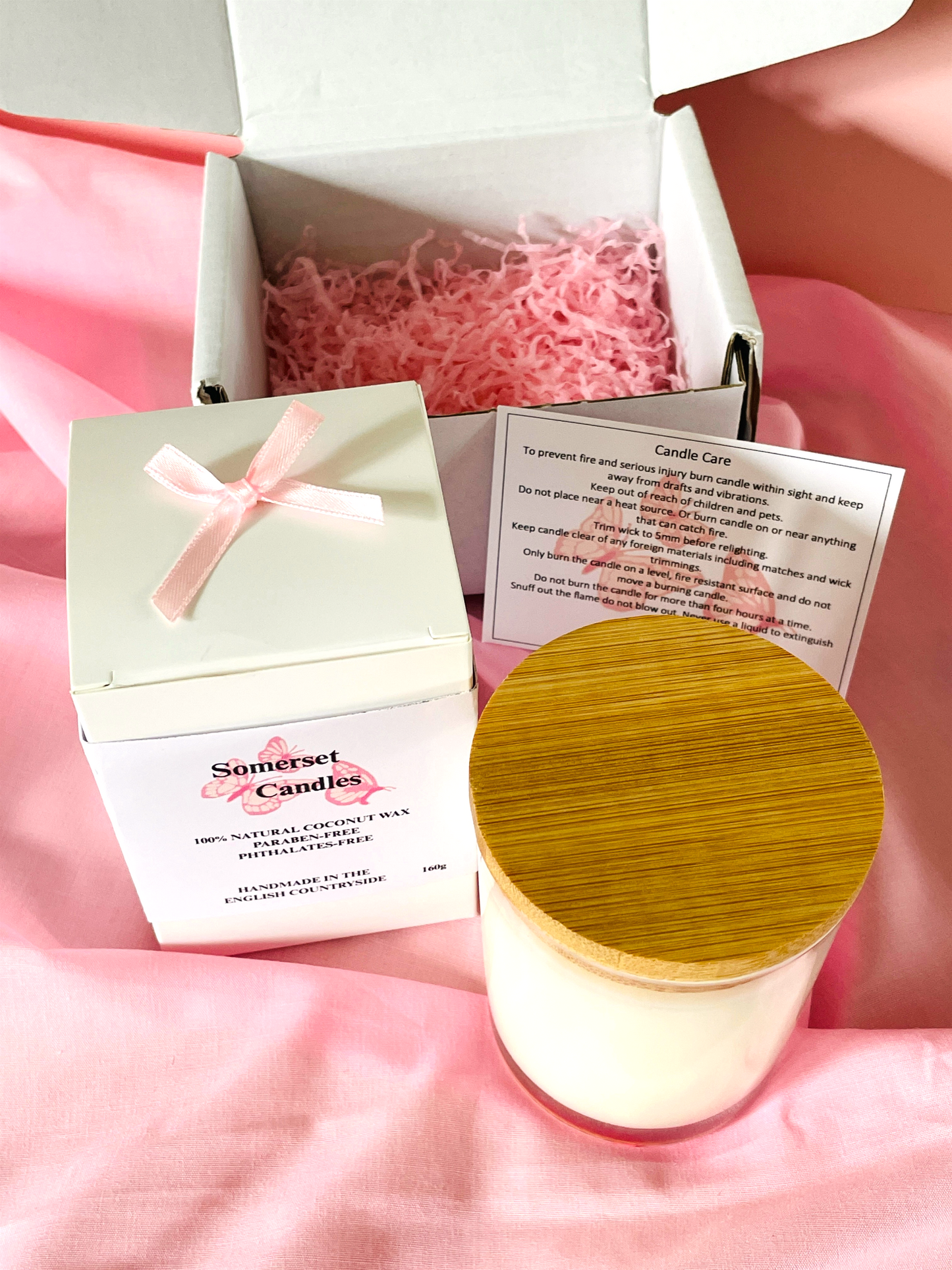 Candle with wooden lid and packaging on a pink fabric background