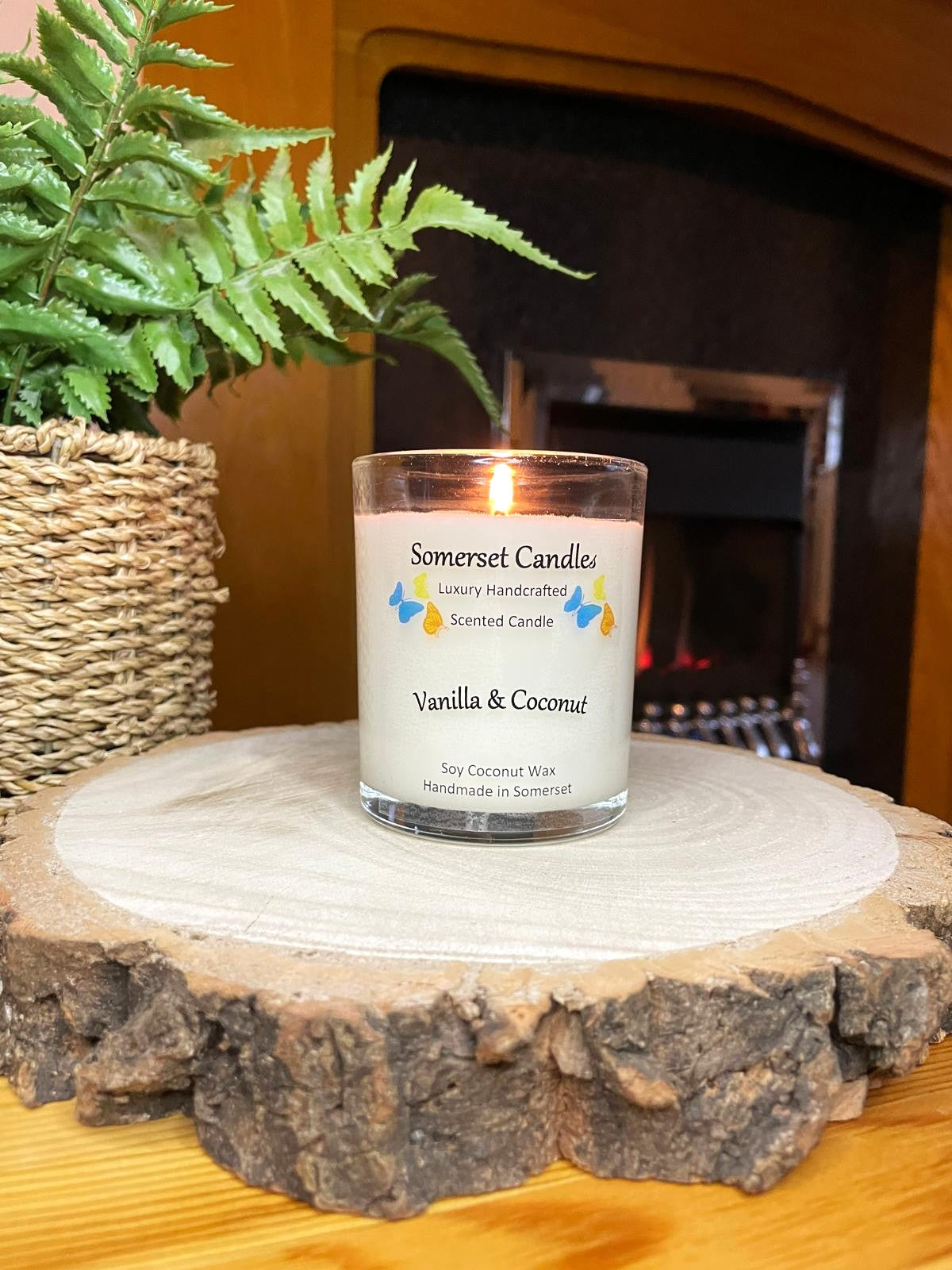 White soy candle in a 7oz clear glass jar with a natural wooden lid. The candle is made from a soy-coconut blend and scented with a fresh scent of vanilla and coconut. Above the scent name on the label, several blue, yellow and orange butterflies are displayed, adding a romantic touch. Clean, minimalist design ideal for gifts, home decor or self-care.