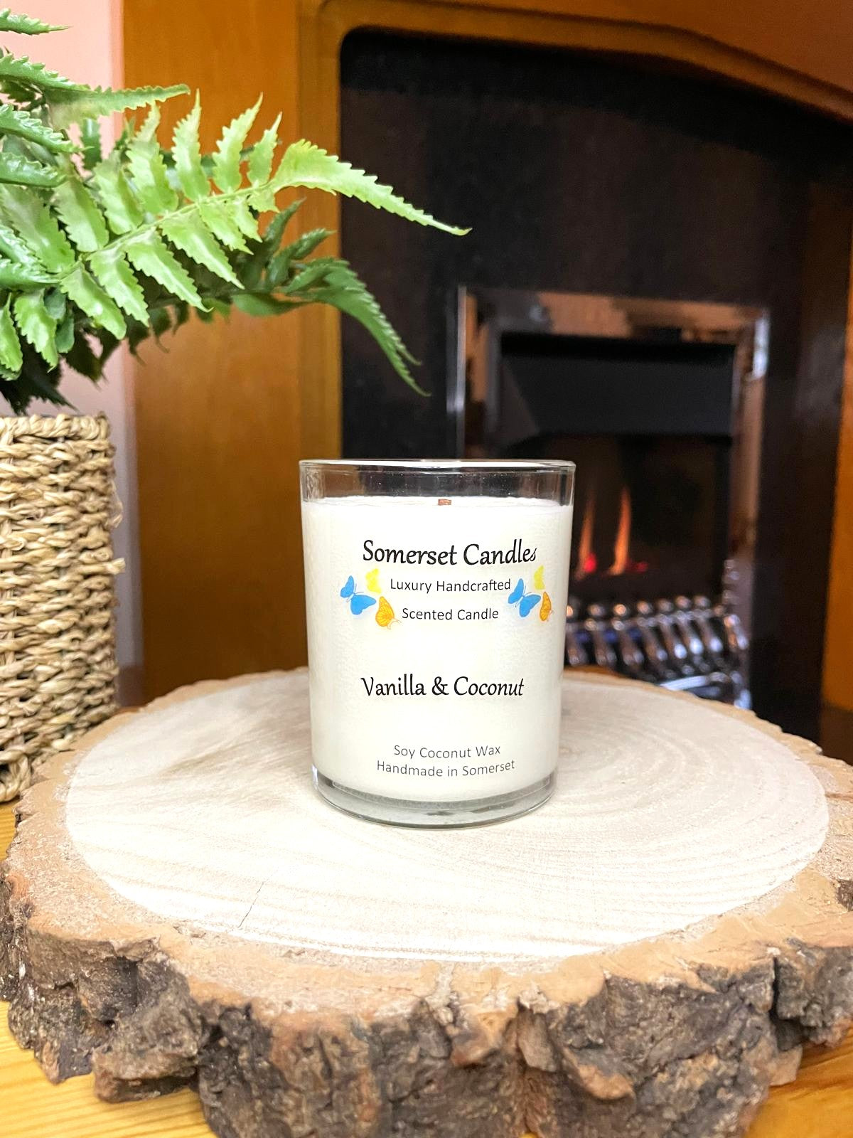 White soy candle in a 7oz clear glass jar with a natural wooden lid. The candle is made from a soy-coconut blend and scented with a fresh scent of vanilla and coconut. Above the scent name on the label, several blue, yellow and orange butterflies are displayed, adding a romantic touch. Clean, minimalist design ideal for gifts, home decor or self-care.