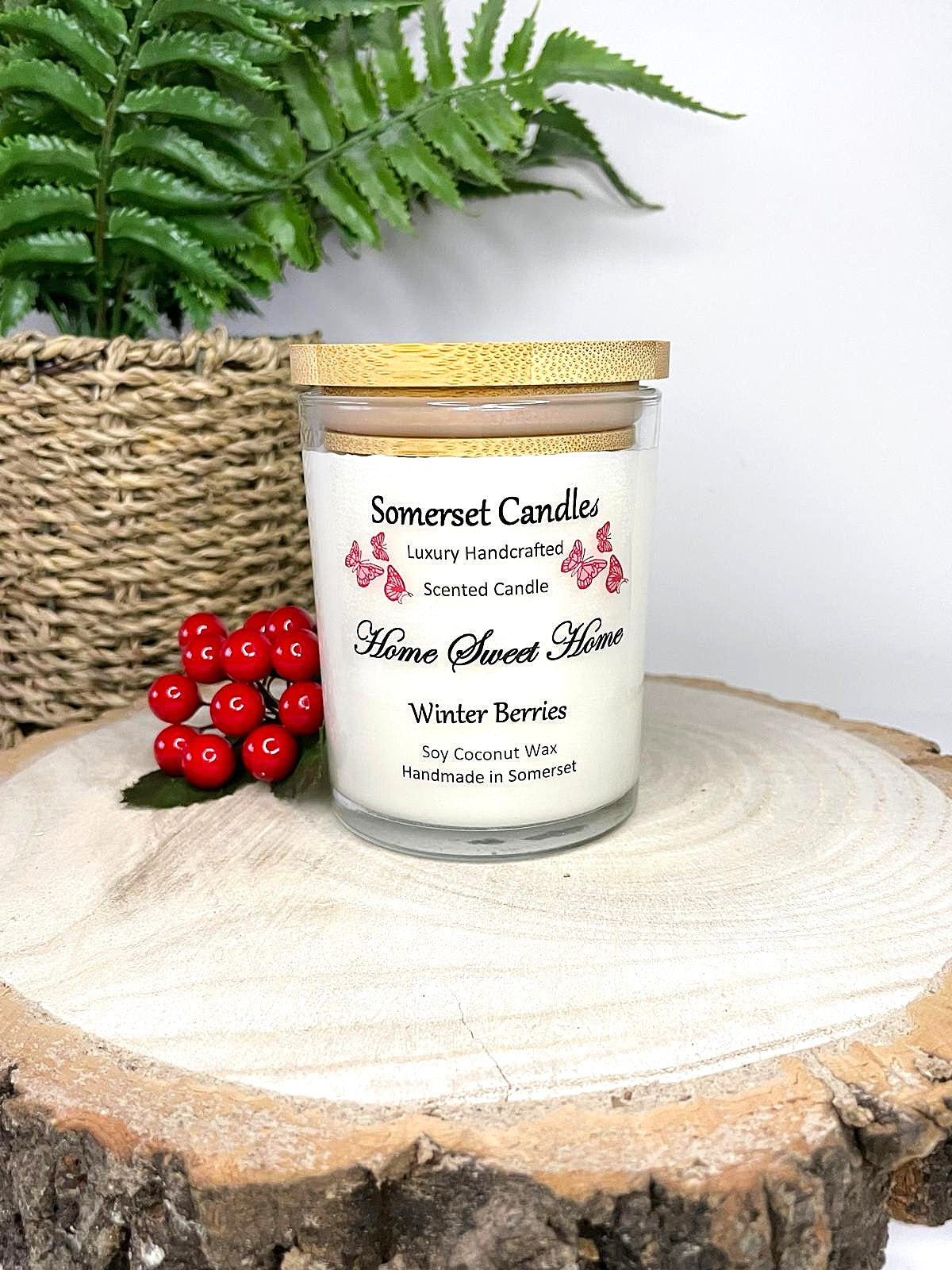 White soy candle in a 7oz clear glass jar with a natural wooden lid. The candle is made from a soy-coconut blend and scented with fruity winter berries. Above the scent name on the label, several red butterflies are displayed, adding a romantic touch. Clean, minimalist design ideal for gifts, home decor or self-care.