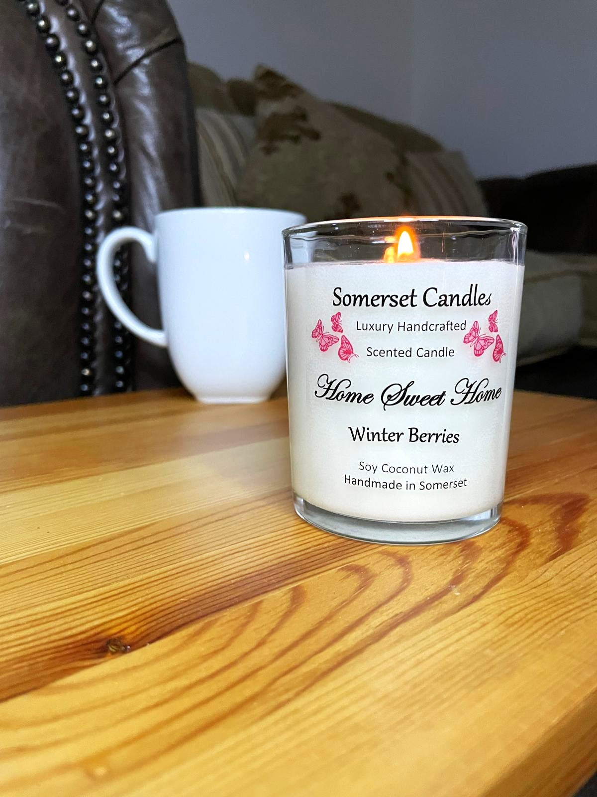 White soy candle in a 7oz clear glass jar with a natural wooden lid. The candle is made from a soy-coconut blend and scented with fruity winter berries. Above the scent name on the label, several red butterflies are displayed, adding a romantic touch. Clean, minimalist design ideal for gifts, home decor or self-care.