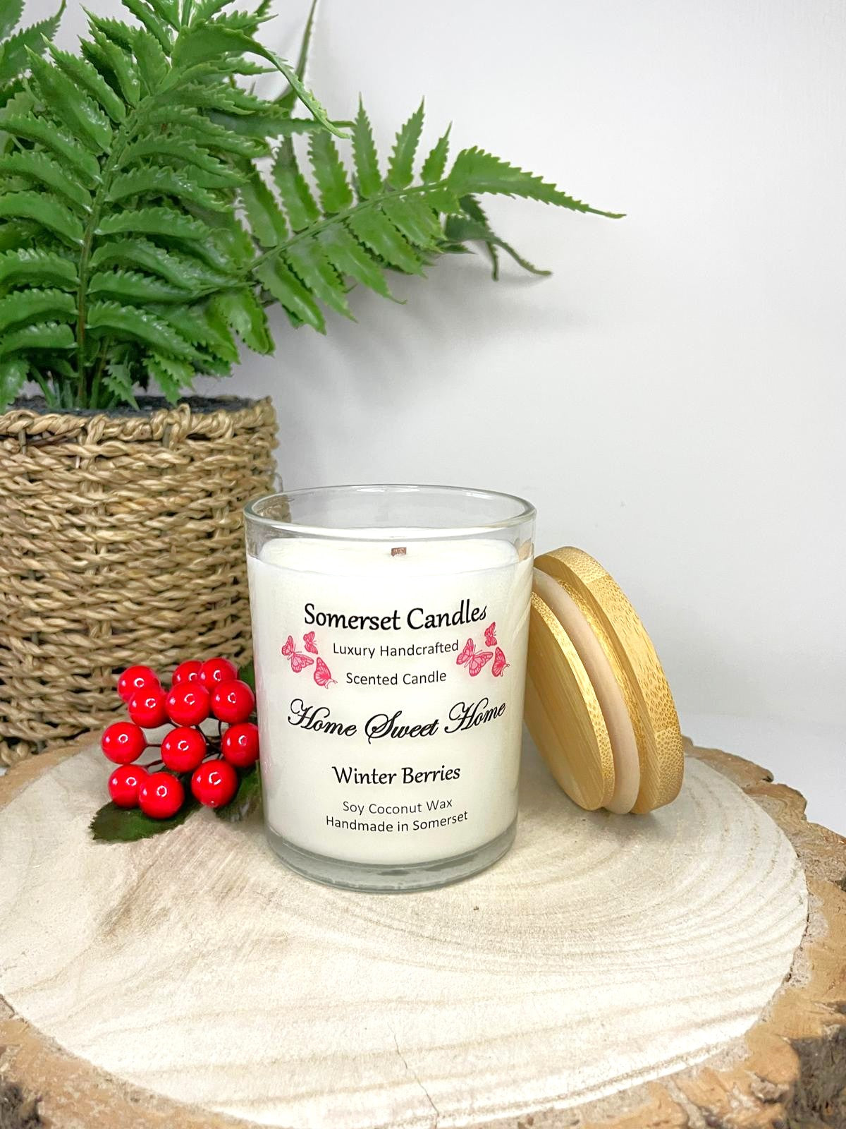 White soy candle in a 7oz clear glass jar with a natural wooden lid. The candle is made from a soy-coconut blend and scented with fruity winter berries. Above the scent name on the label, several red butterflies are displayed, adding a romantic touch. Clean, minimalist design ideal for gifts, home decor or self-care.