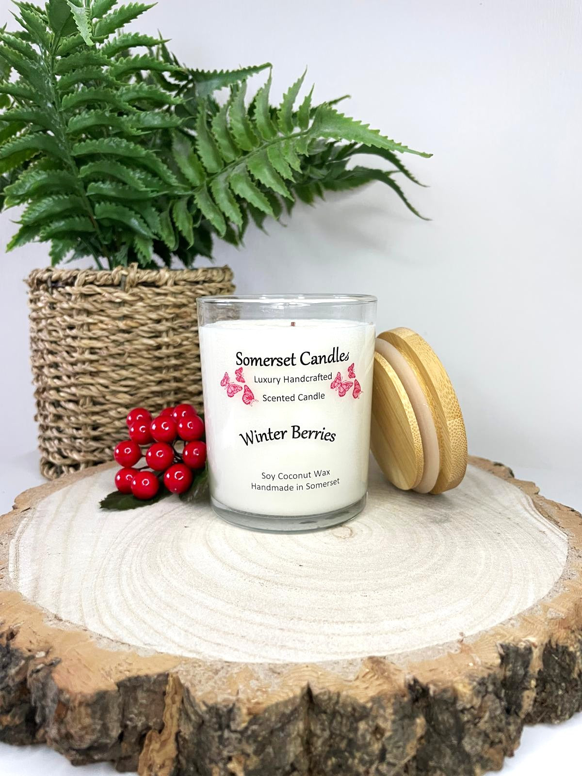 White soy candle in a 7oz clear glass jar with a natural wooden lid. The candle is made from a soy-coconut blend and scented with a fruity scent of winter berries. Above the scent name on the label, several red butterflies are displayed, adding a romantic touch. Clean, minimalist design ideal for gifts, home decor or self-care.