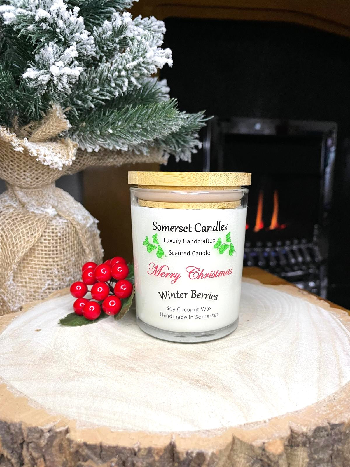 White soy candle in a 7oz clear glass jar with a natural wooden lid. The candle is made from a soy-coconut blend and scented with a fruity scent of winter berries. Above the scent name on the label, several red butterflies are displayed, adding a romantic touch. Clean, minimalist design ideal for gifts, home decor or self-care.