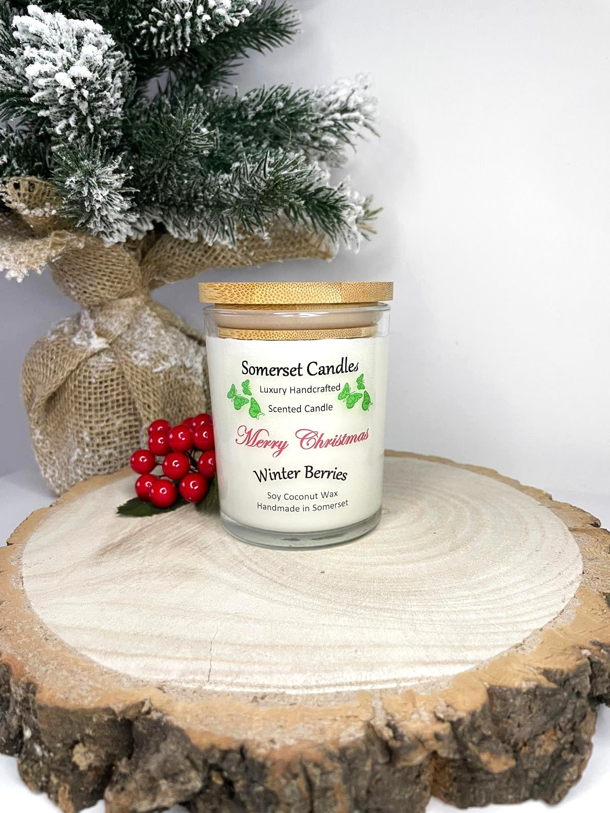 White soy candle in a 7oz clear glass jar with a natural wooden lid. The candle is made from a soy-coconut blend and scented with a fruity scent of winter berries. Above the scent name on the label, several red butterflies are displayed, adding a romantic touch. Clean, minimalist design ideal for gifts, home decor or self-care.