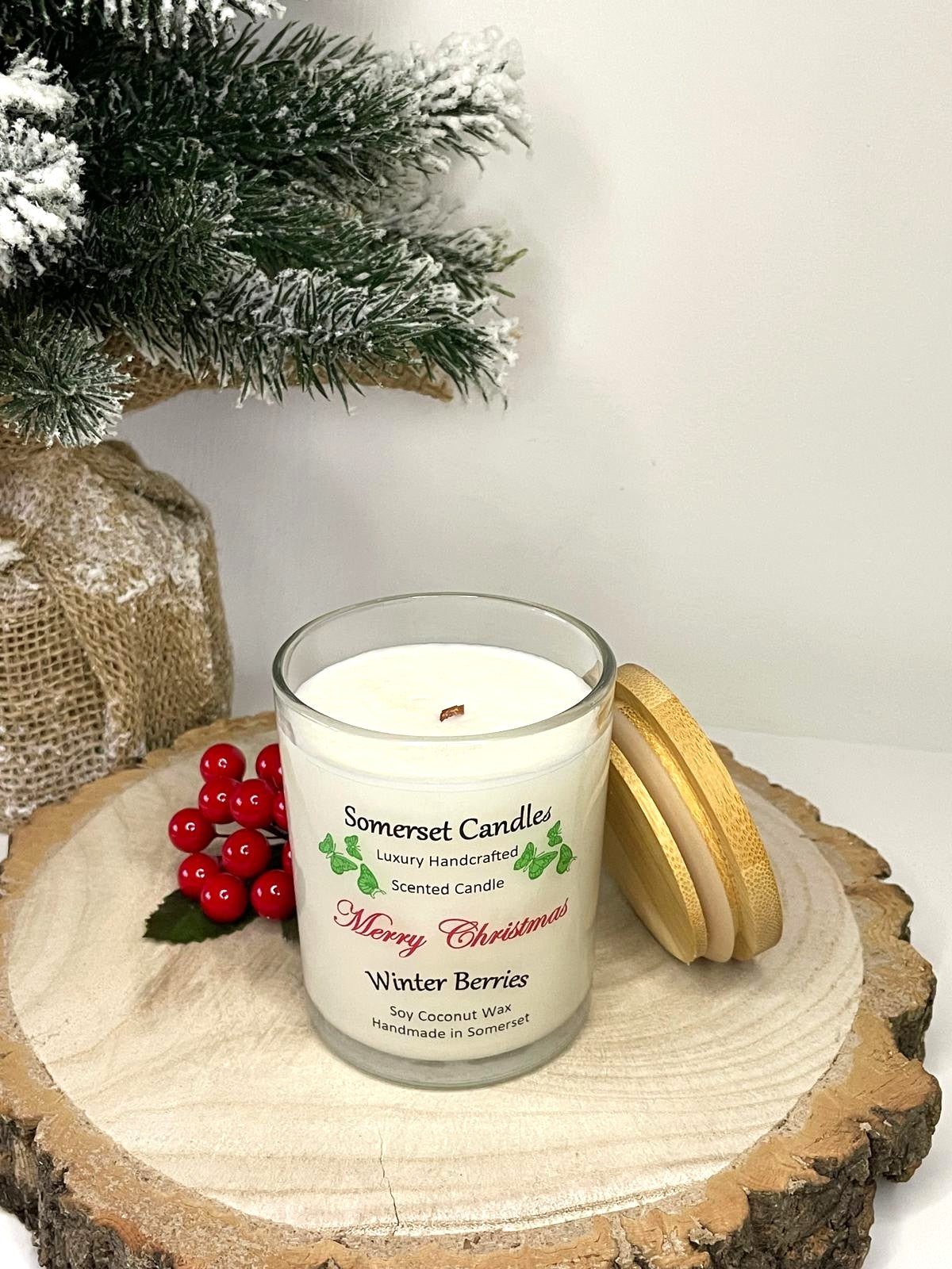 White soy candle in a 7oz clear glass jar with a natural wooden lid. The candle is made from a soy-coconut blend and scented with a fruity scent of winter berries. Above the scent name on the label, several red butterflies are displayed, adding a romantic touch. Clean, minimalist design ideal for gifts, home decor or self-care.