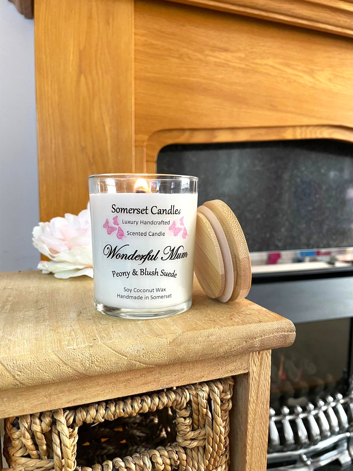 White soy candle in a 7oz clear glass jar with a natural wooden lid. The candle is made from a soy-coconut blend and scented with a delicate mix of peony and blush suede. Above the scent name on the label, several pink butterflies are displayed, adding a romantic touch. Clean, minimalist design ideal for gifts, home decor or self-care.