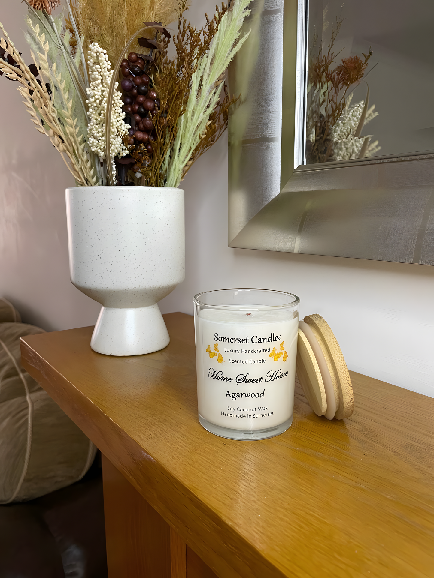 Home Sweet Home Agarwood soy candle is displayed on the mantelpiece with autumn flowers. The candle is white in colour with orange butterflies fluttering above the scent name and fitted with a lovely bamboo lid.