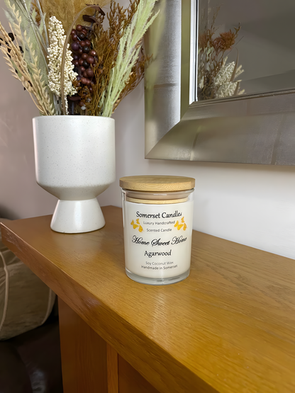 Home Sweet Home Agarwood soy candle is displayed on the mantelpiece with autumn flowers. The candle is white in colour with orange butterflies fluttering above the scent name and fitted with a lovely bamboo lid.