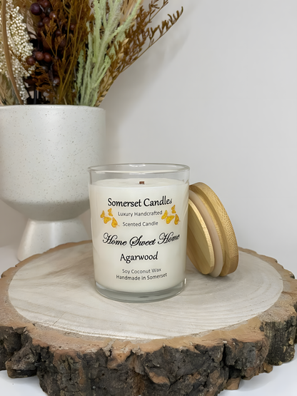 Home Sweet Home Agarwood soy candle is displayed on a wooden board with autumn flowers. The candle is white in colour with orange butterflies fluttering above the scent name and fitted with a lovely bamboo lid.