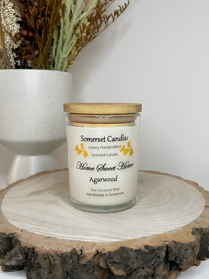 Home Sweet Home Agarwood soy candle is displayed on a wooden board with autumn flowers. The candle is white in colour with orange butterflies fluttering above the scent name and fitted with a lovely bamboo lid.