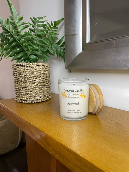 Agarwood soy candle displayed on the mantelpiece. The candle is white in colour with bright orange butterflies above the scent name with a lovely bamboo lid. The candle jar is clear glass.