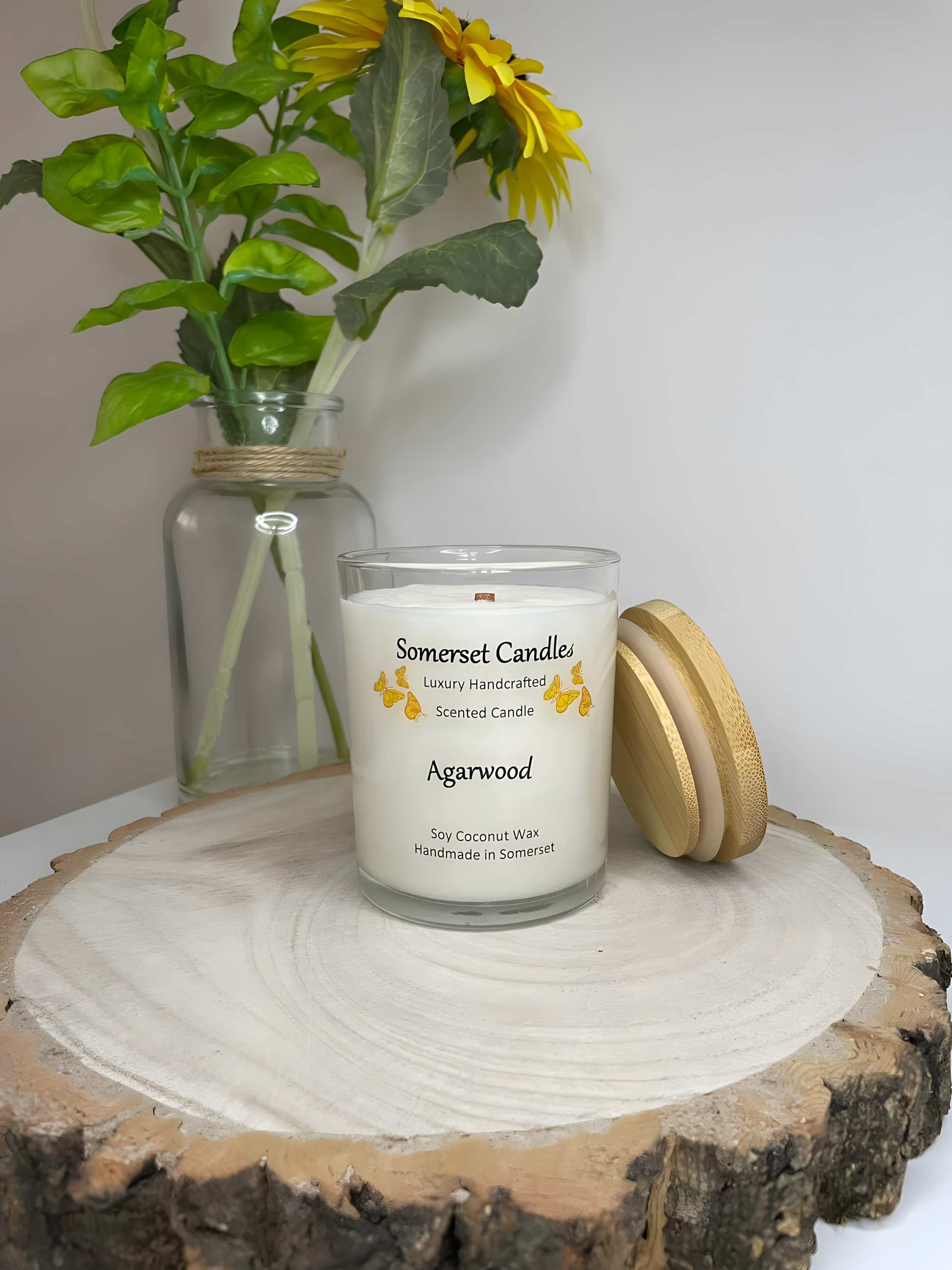 Agarwood soy candle displayed on a wooden board. The candle is white in colour with bright orange butterflies above the scent name with a lovely bamboo lid. The candle jar is clear glass.